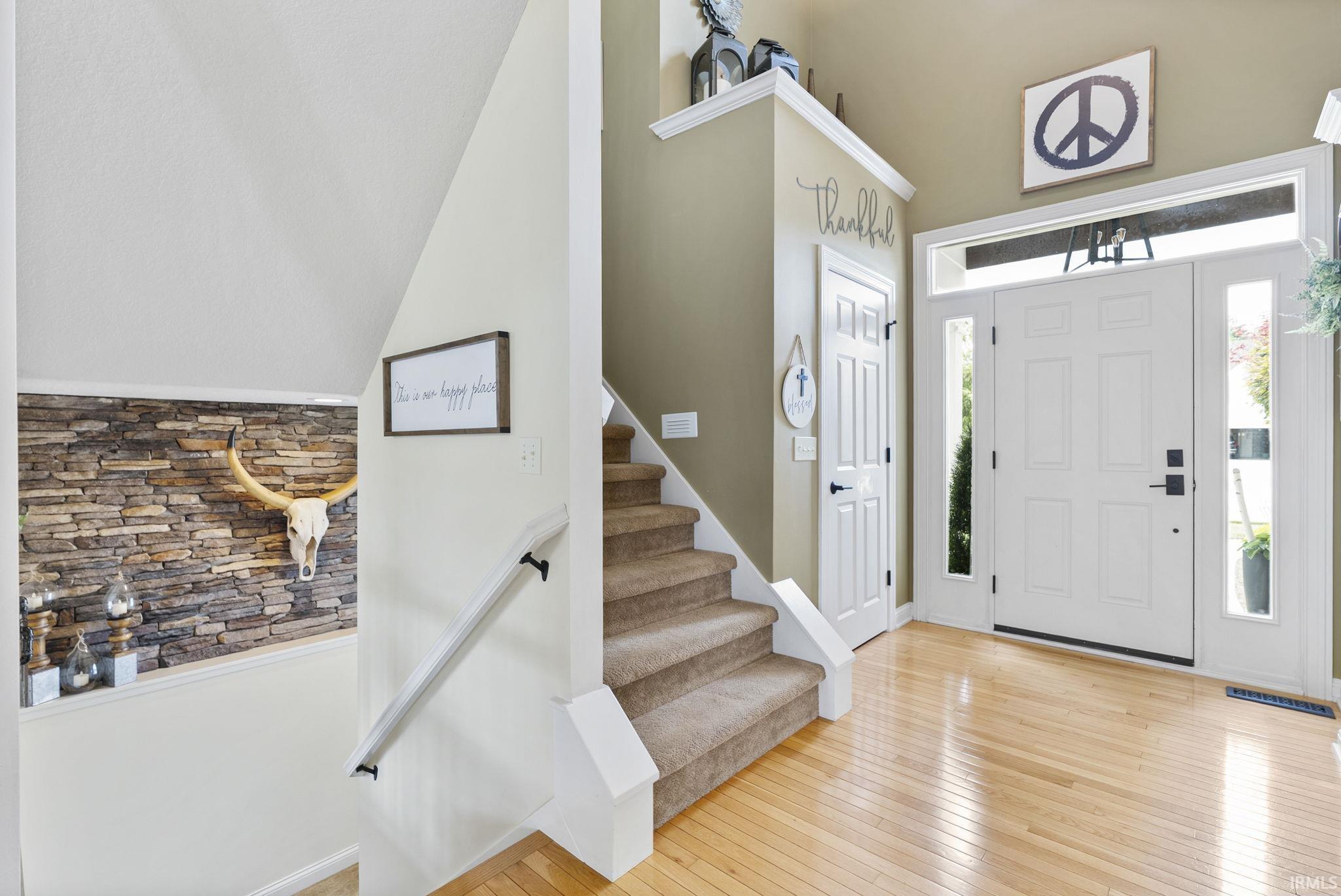 Welcoming foyer featuring a striking stacked-stone accent wall, wide-plank wood-finish flooring, and a gracefully curved staircase with white painted railings and metal handrails