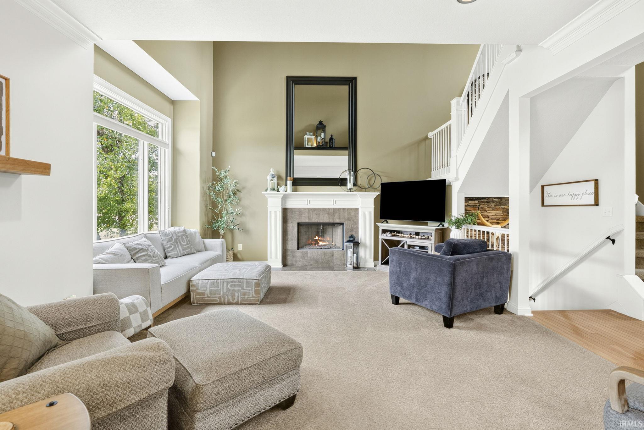 Living space featuring a fireplace with a mantel, large windows, and a staircase with white balusters