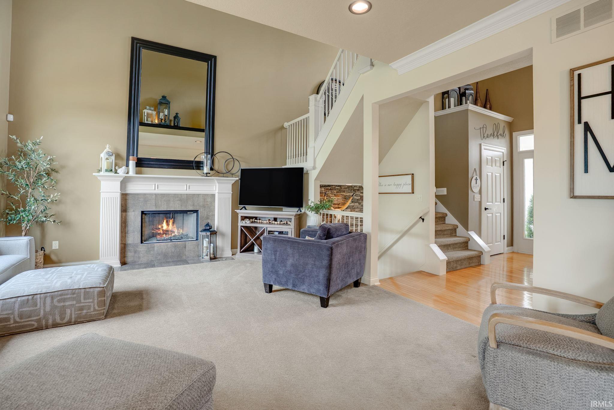 Living area featuring a floor-to-ceiling fireplace with a tile surround and white mantle, carpeted flooring, and high ceilings