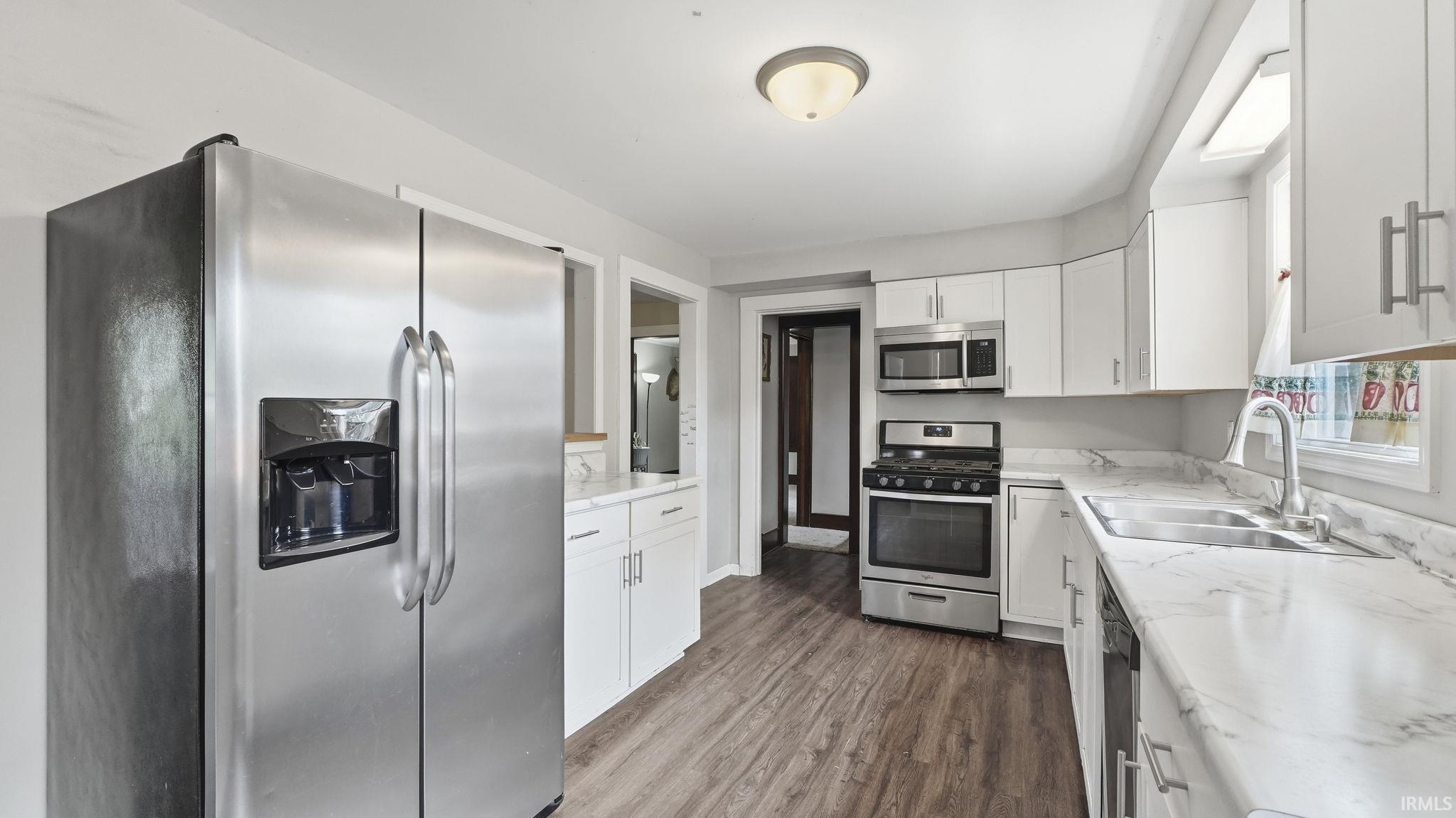 Kitchen featuring stainless steel appliances, white cabinetry, wood-finish flooring, and light-toned countertops