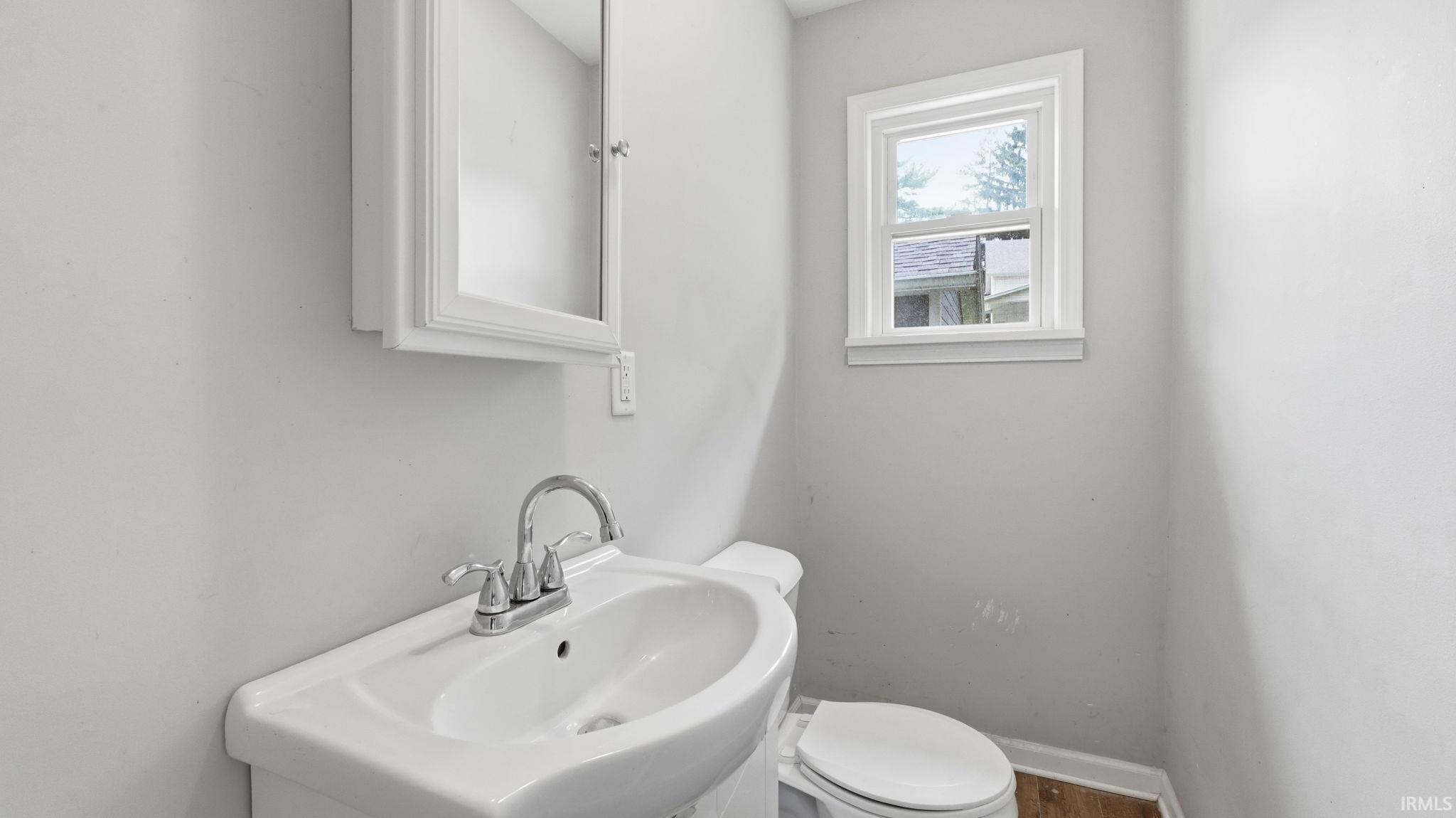 Pedestal sink with chrome faucet, white medicine cabinet, and window with white trim