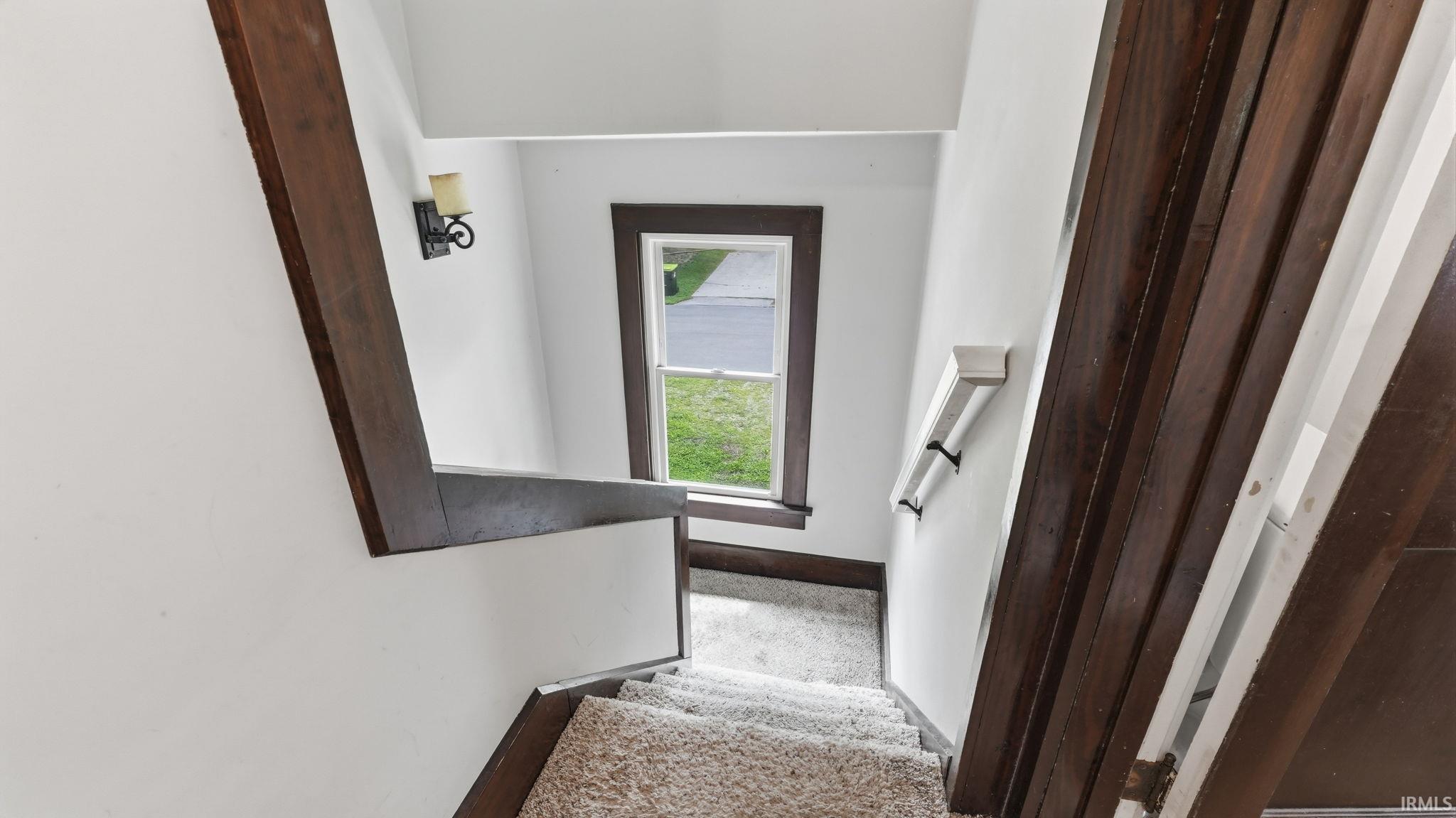 Staircase featuring carpeted treads, dark wood trim, a single window, and a wall-mounted sconce