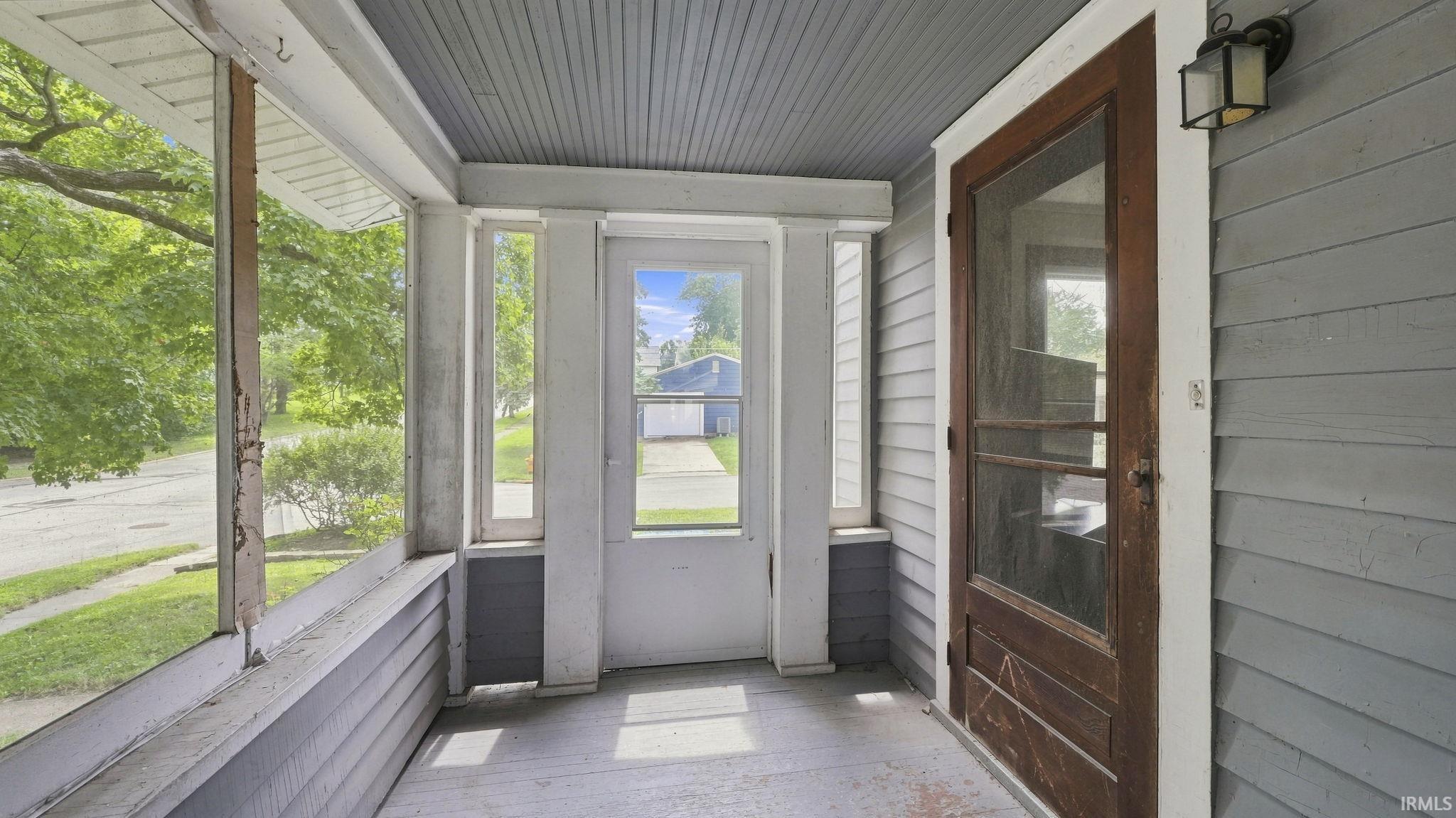 Screened-in front porch featuring a wood-finish screen door, horizontal siding, and a ceiling-mounted light fixture