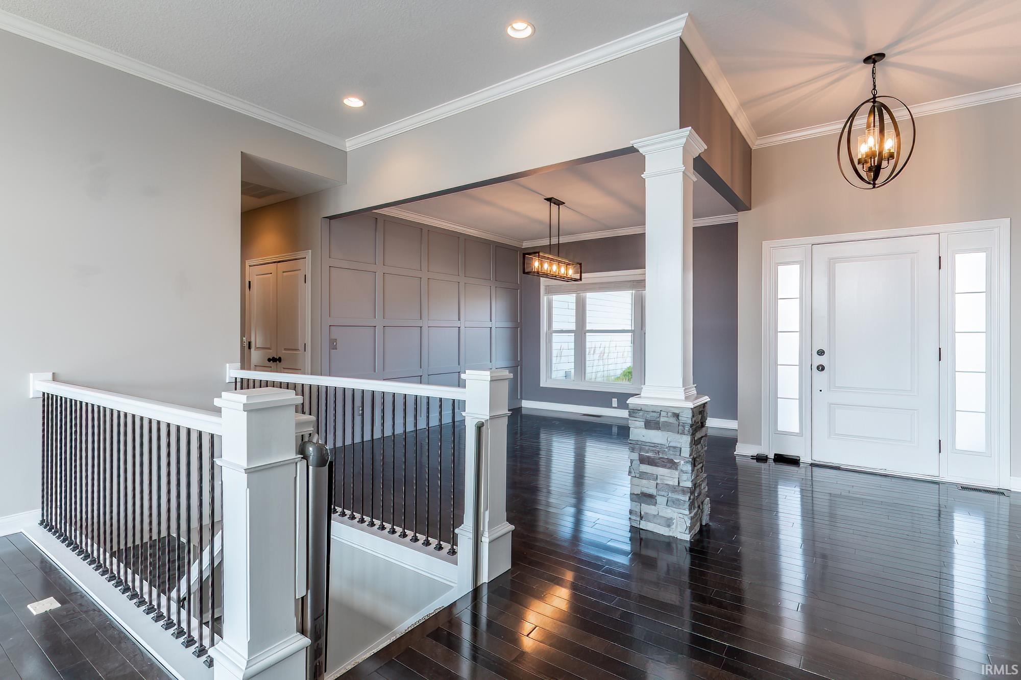 Foyer featuring dark wood-finish flooring, a white paneled entry door with sidelights, a decorative light fixture, and a stone-clad column