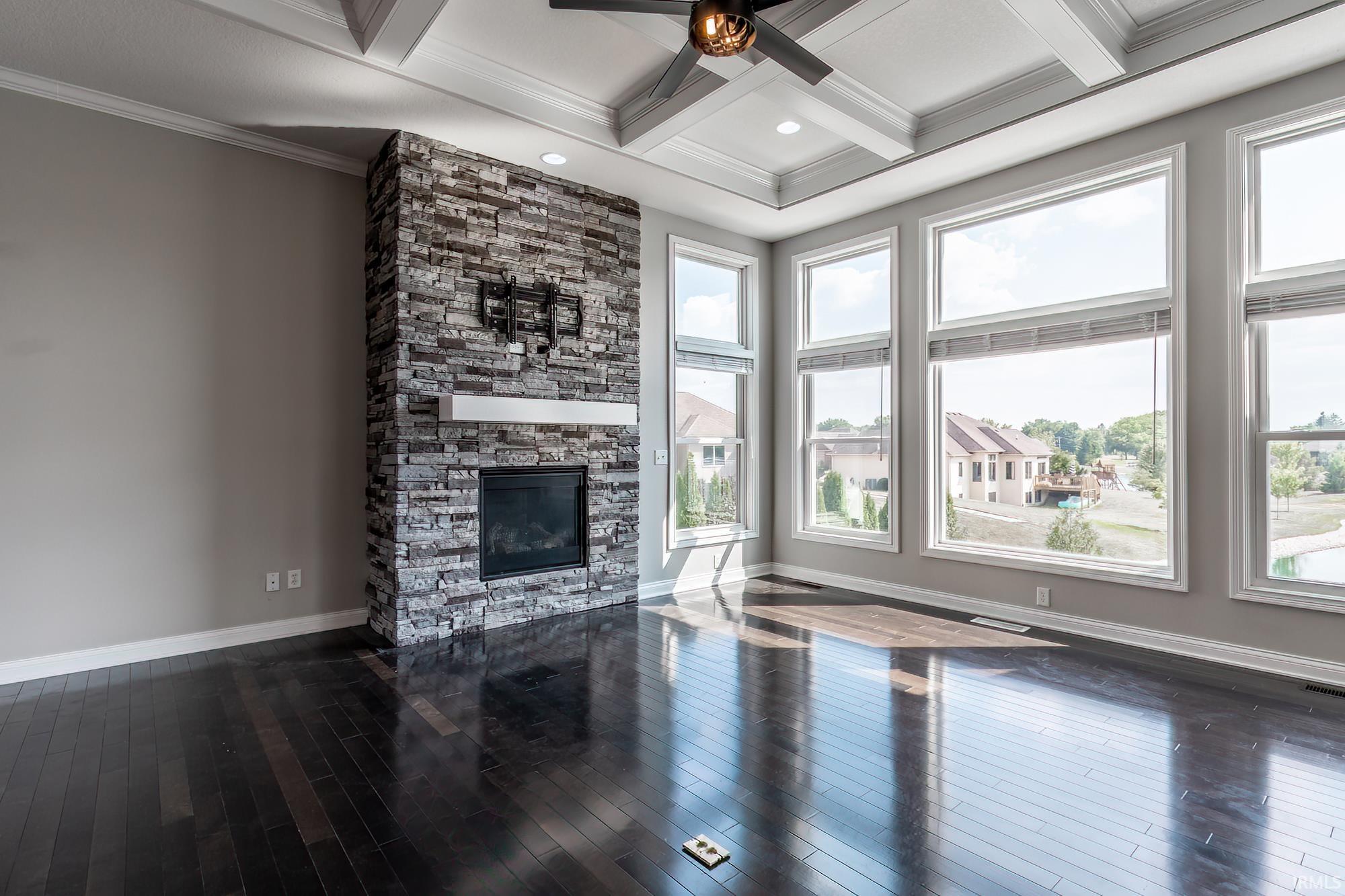 Living space featuring a stone-clad fireplace with a white mantel, dark wood-finish flooring, a coffered ceiling with a ceiling fan, recessed lighting, and multiple large windows