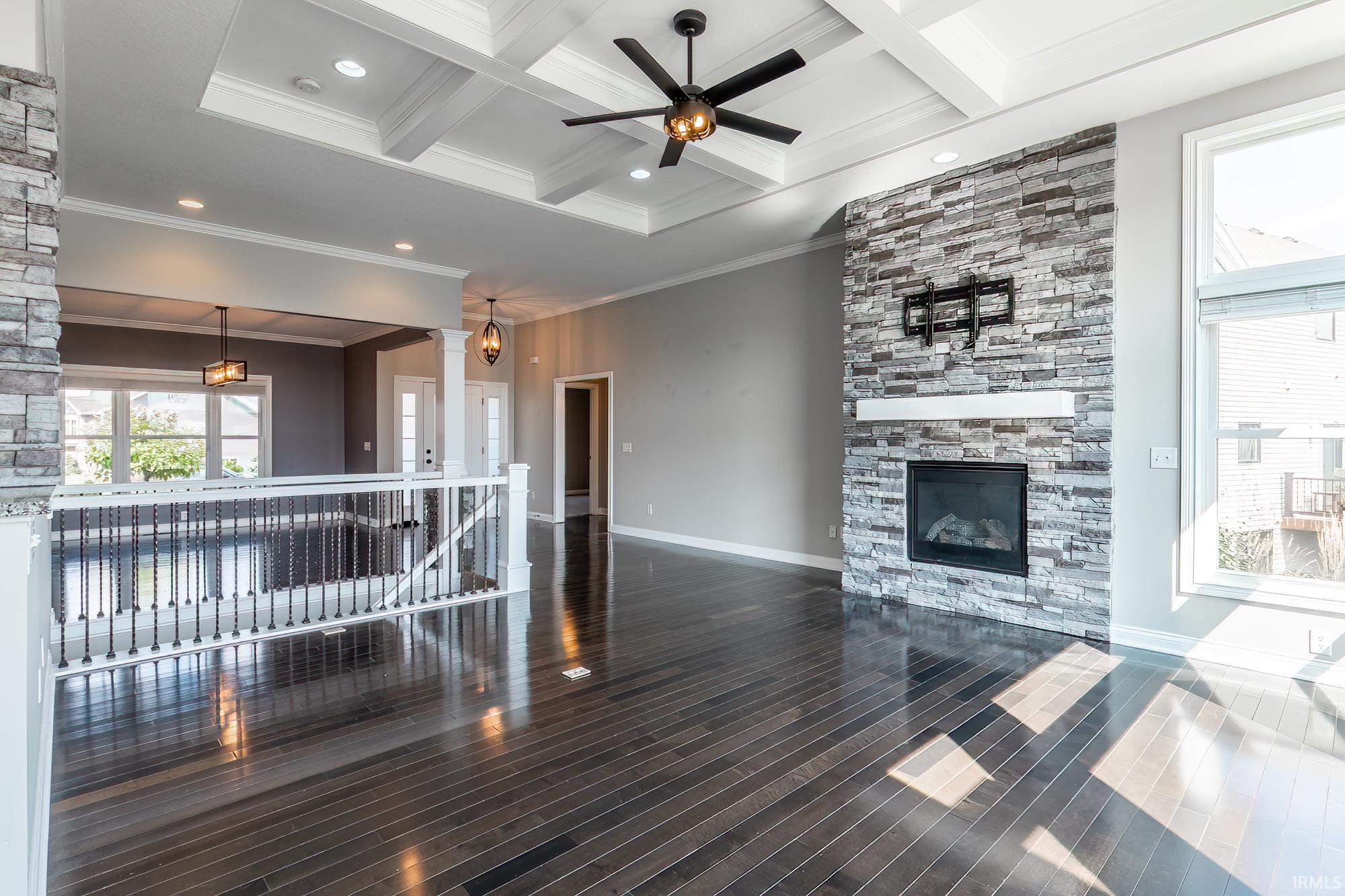 Spacious room featuring dark wood-finish flooring, a stacked stone fireplace with a white mantel, and a coffered ceiling with a ceiling fan