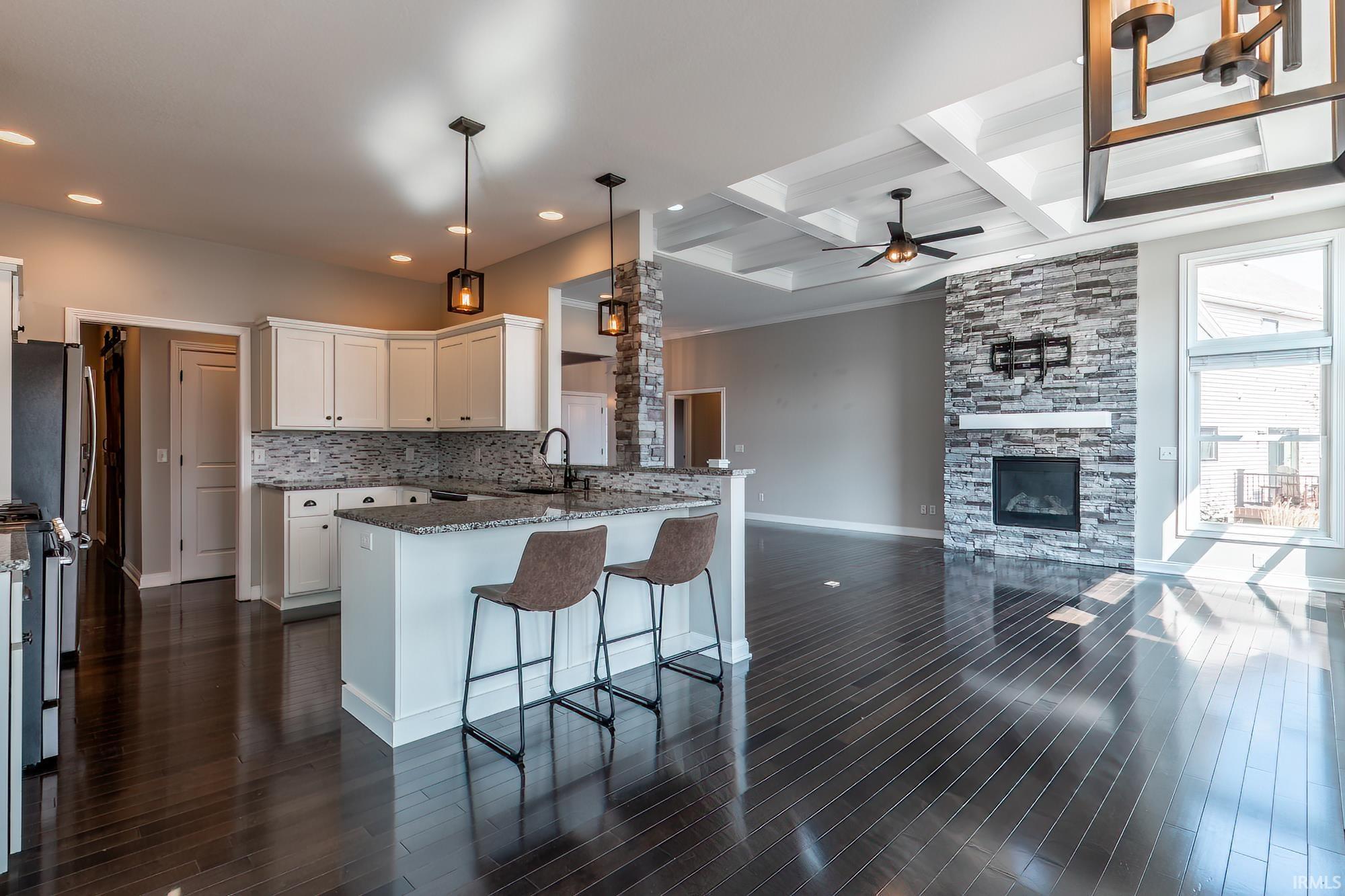 Open-concept main living area featuring wood-finish flooring, a stone-faced fireplace with white mantel, and a coffered ceiling