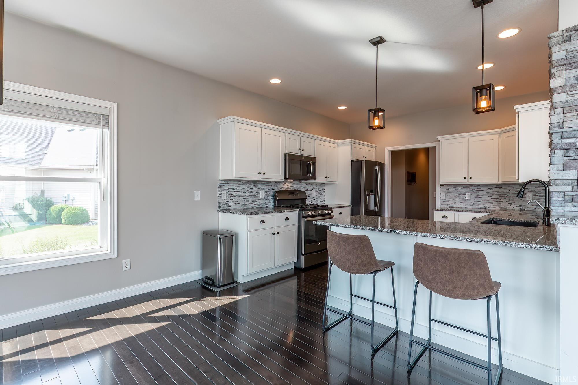 Kitchen featuring white cabinetry, dark wood-finish flooring, a stone veneer accent wall, pendant lighting, and an island with a countertop
