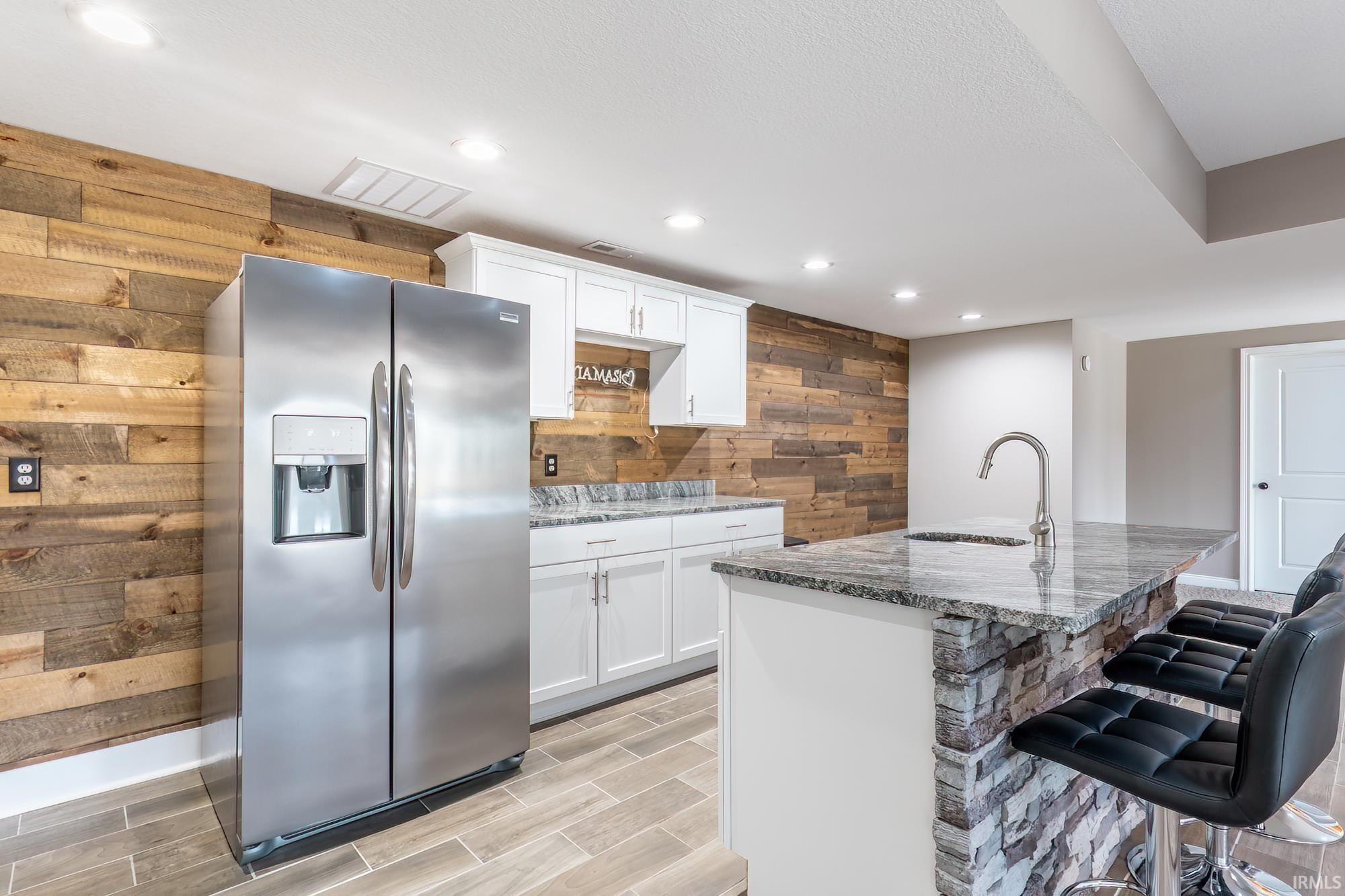 Kitchenette featuring a stone-clad island with granite countertop and integrated sink, white shaker-style cabinetry, and a full-size stainless steel refrigerator