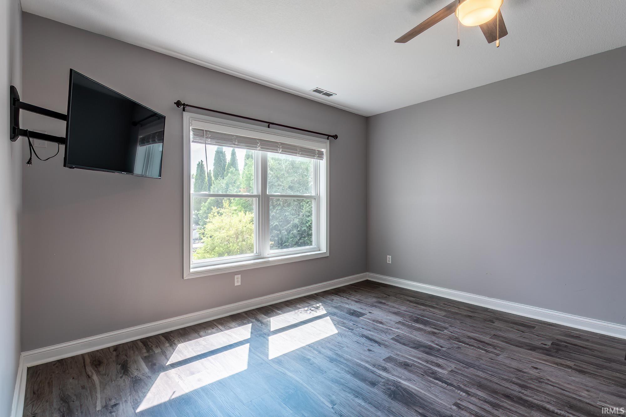 Room featuring wood-finish flooring, a double window with blinds, and light gray wall paint