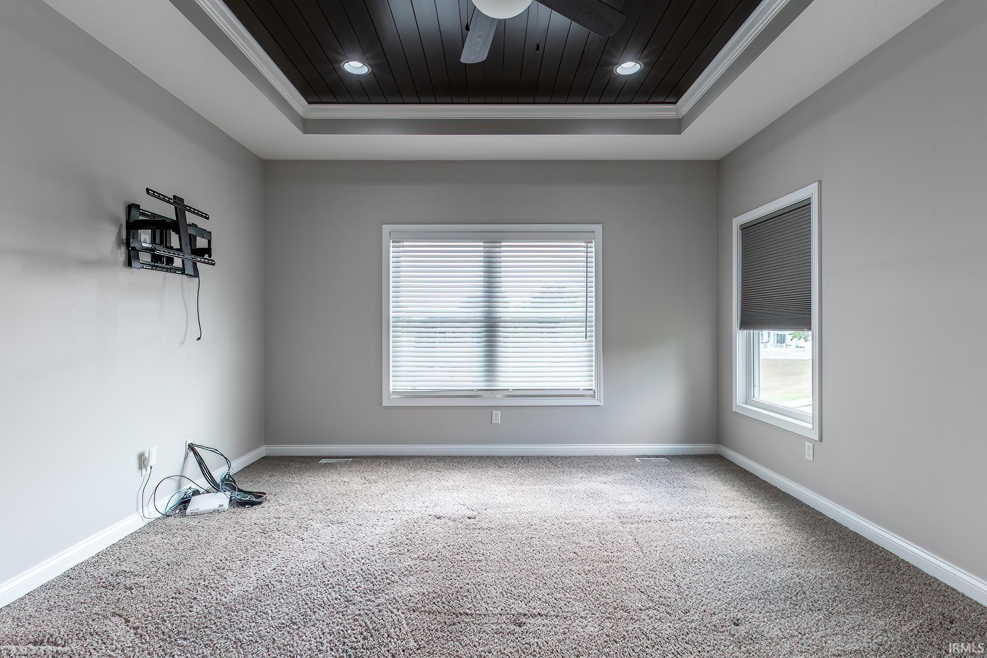 Spacious bedroom featuring neutral wall finishes, recessed ceiling lighting with dark wood-finish soffit detail, and dual windows with cellular blinds providing natural light and privacy