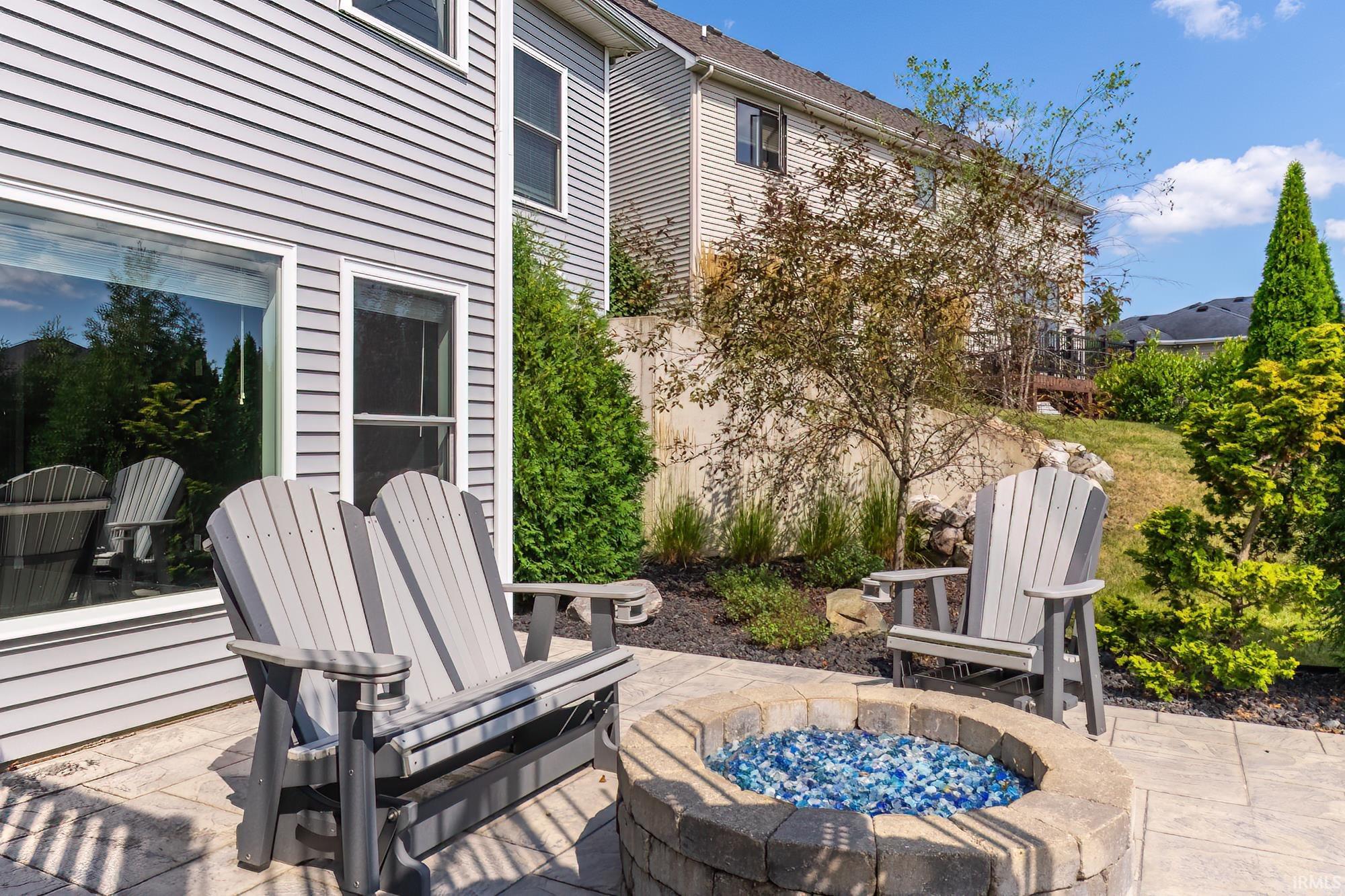 Outdoor entertaining space featuring two Adirondack chairs, a stone-surround fire pit, and a paver patio