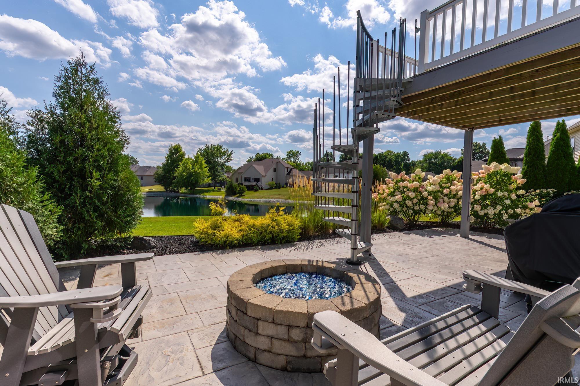 Expansive patio featuring a circular fire pit with decorative stone surround, multiple Adirondack seating, and a covered deck with metal railings overhead