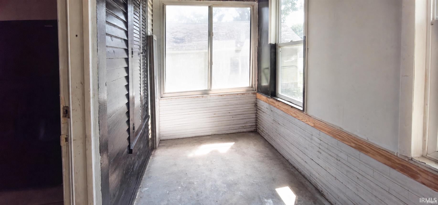 Bright sunroom with expansive glazed windows, wood-finish wainscoting, and concrete flooring