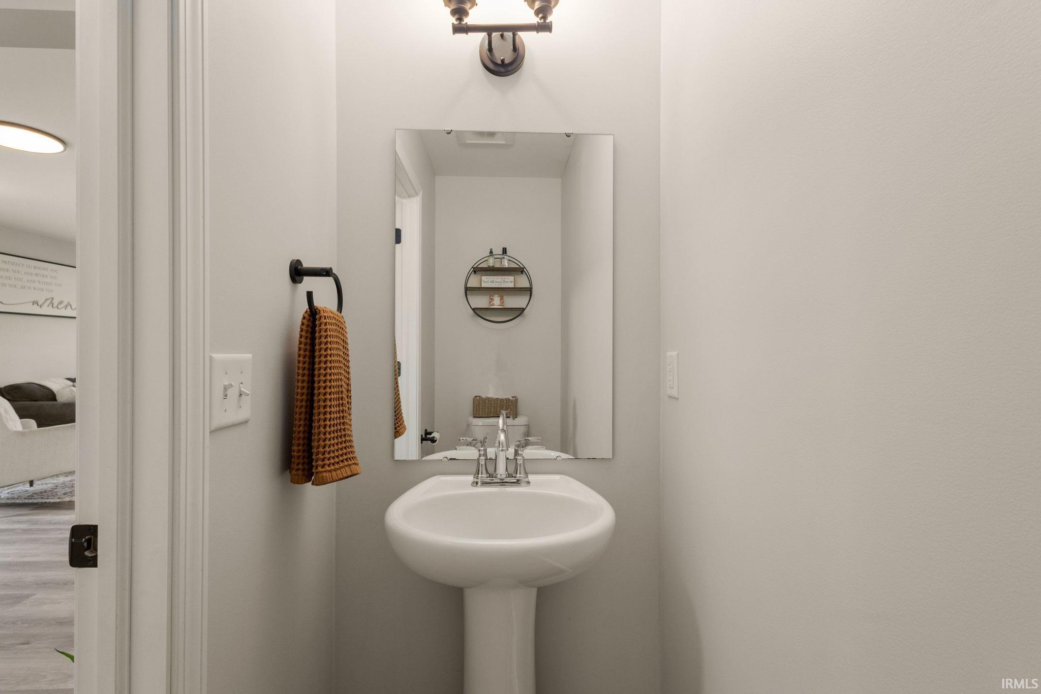 Pedestal sink with chrome faucet, wall-mounted mirror, and overhead vanity light fixture