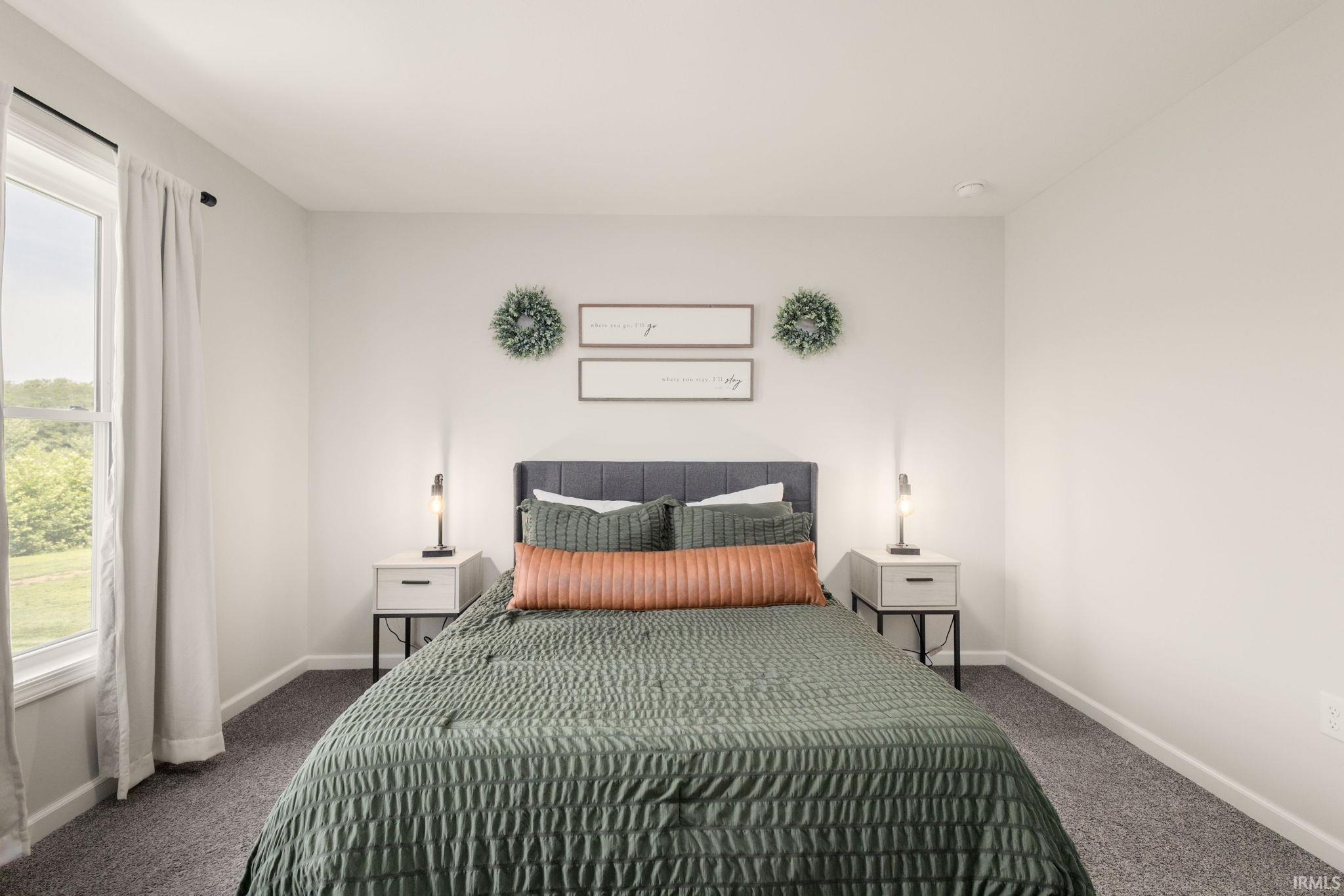 Bedroom featuring a window with exterior landscape, light gray walls, dark gray carpet, and a paneled headboard