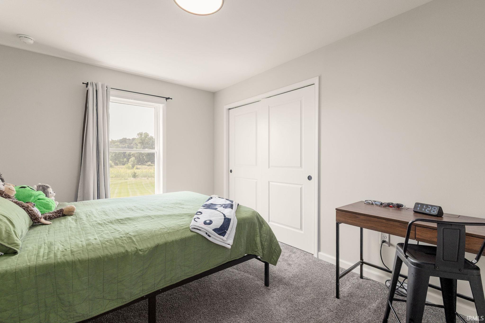 Bedroom with light gray walls, gray carpet flooring, and a window with a green outdoor scenery