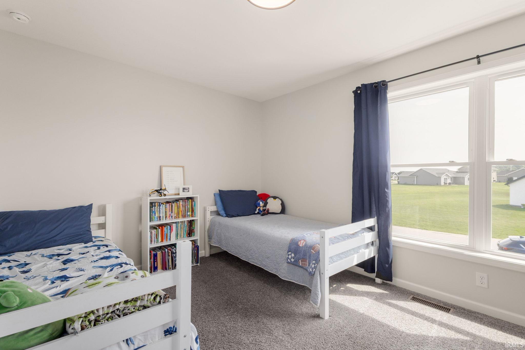 Spacious room featuring neutral painted walls, durable carpet flooring, a large window with white trim, and a ceiling light fixture