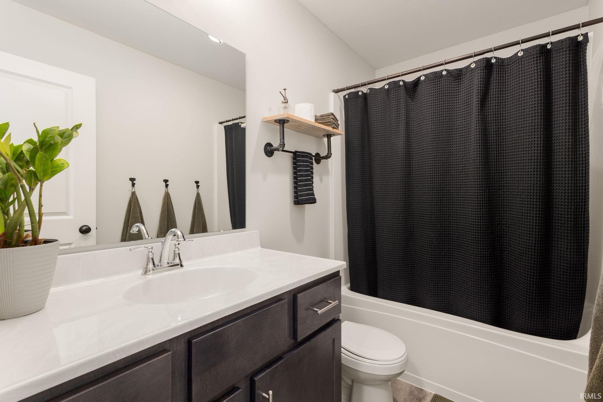 Bathroom featuring a vanity with a white countertop and undermount sink, dark wood-finish cabinetry, a chrome faucet, and a combination tub and shower