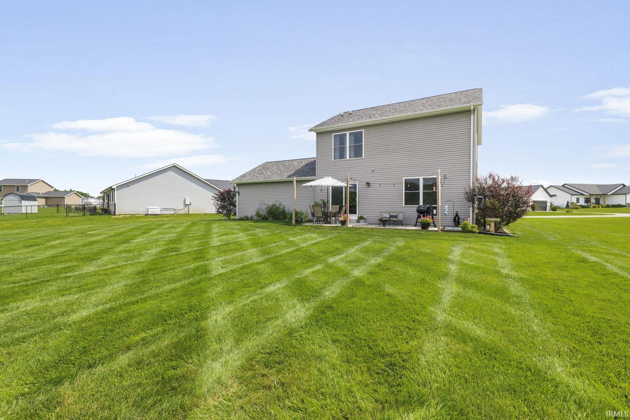 Spacious green lawn with a two-story residence featuring light gray siding and a dark gray shingle roof