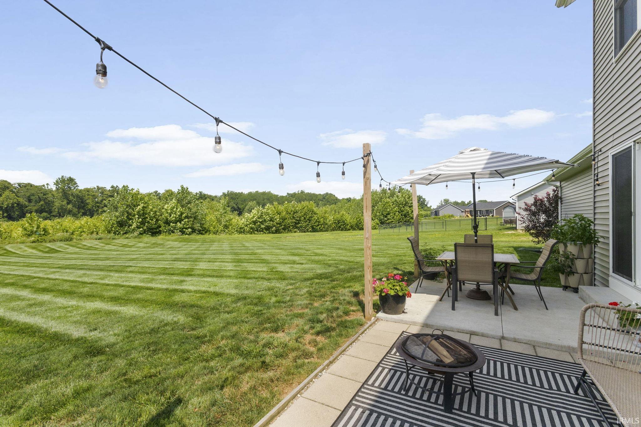 Expansive backyard featuring a manicured lawn, concrete patio, and string lighting