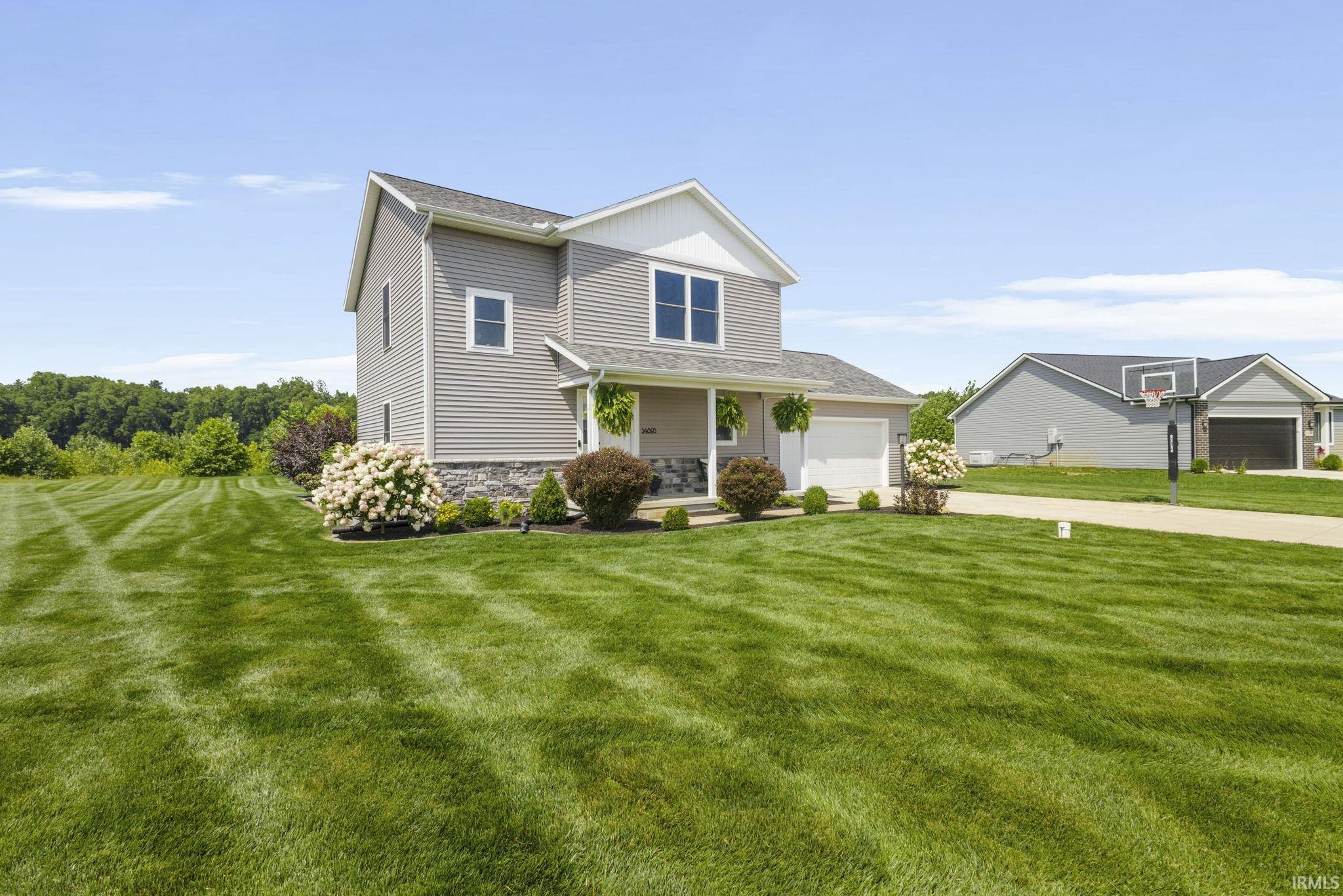 Two-story residence featuring light gray siding, white trim, and a stone facade foundation