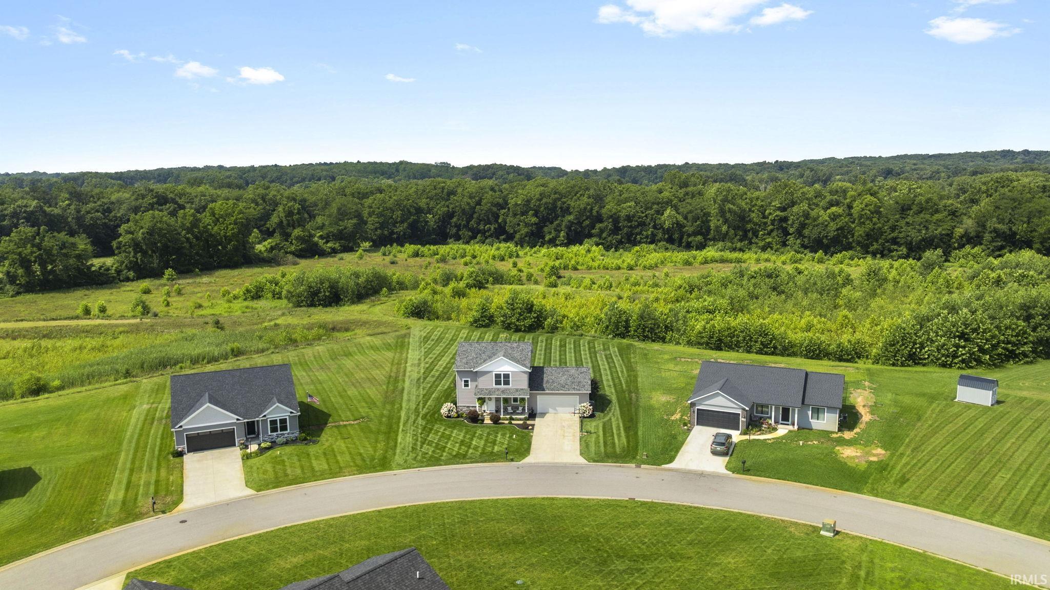 Residential neighborhood featuring modern homes, paved cul-de-sac, manicured lawns, and a natural wooded backdrop