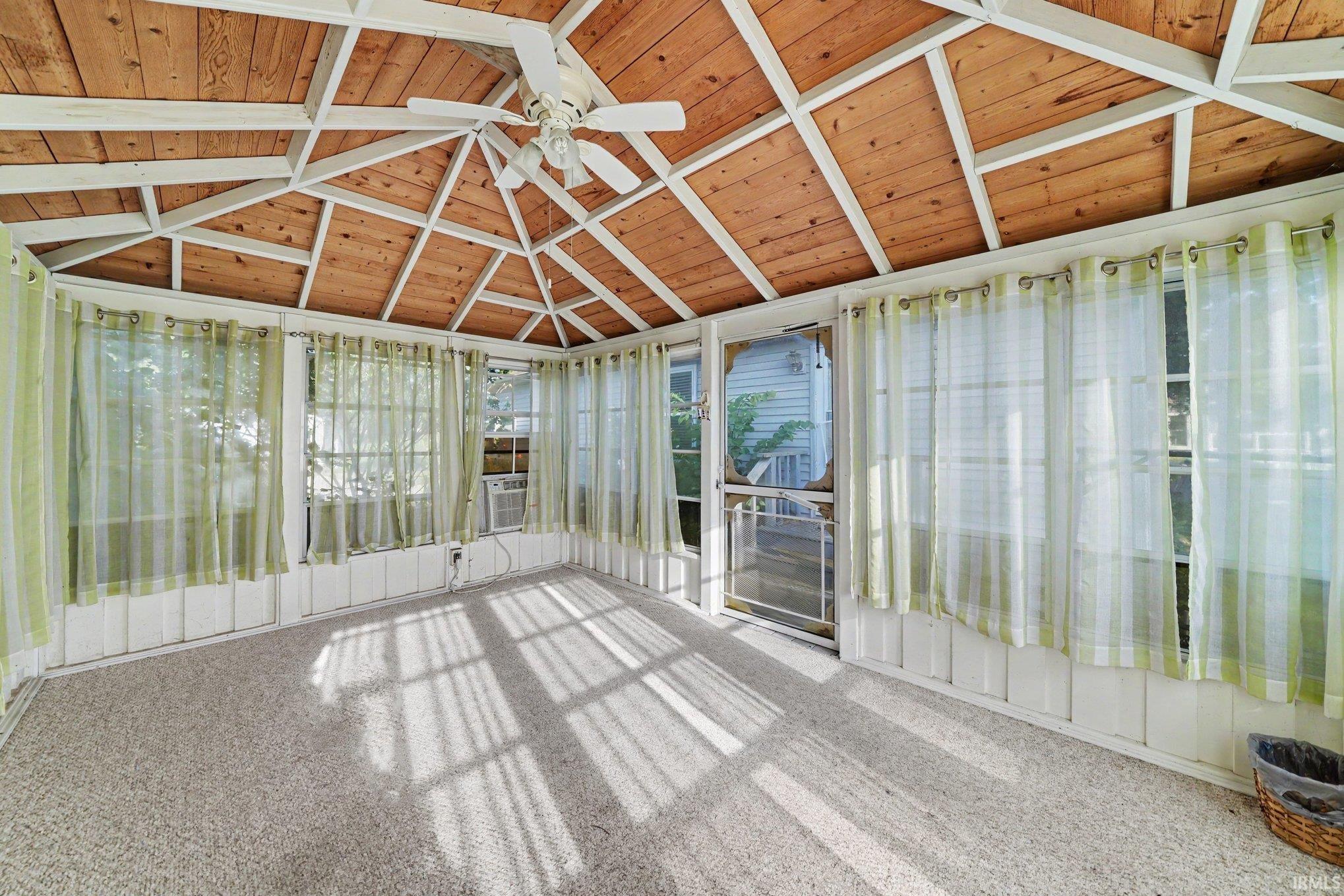 Sunroom featuring a wood-paneled ceiling with exposed white beams, a ceiling fan, and light-colored carpet flooring