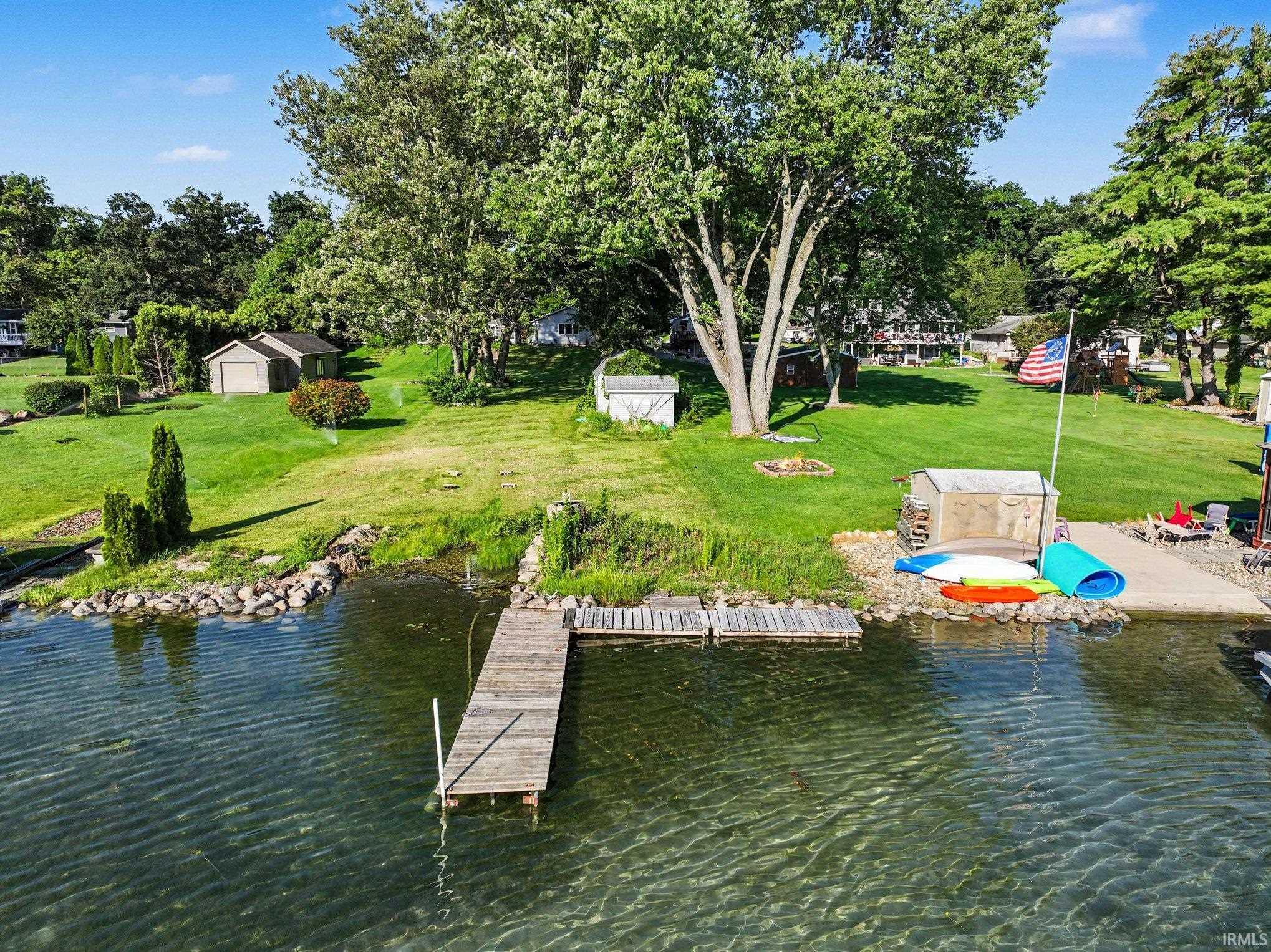 Waterfront property featuring a private dock, concrete boat ramp, expansive lawn, mature trees, and an accessory structure