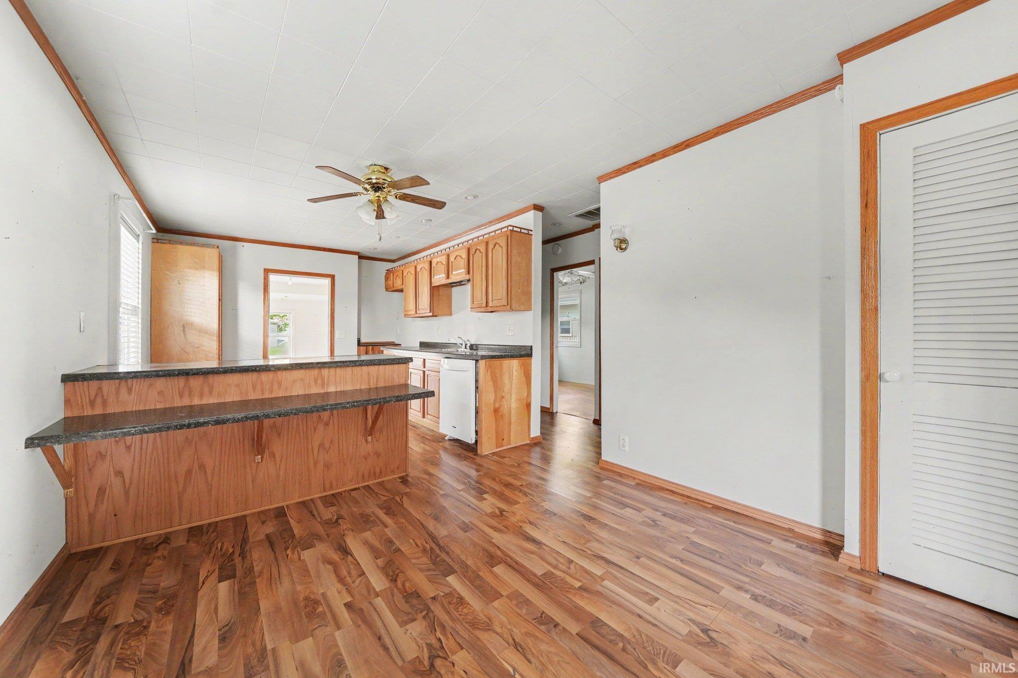 Open concept kitchen and living area featuring wood-finish flooring, a breakfast bar with a dark countertop, wood cabinetry, and a ceiling fan