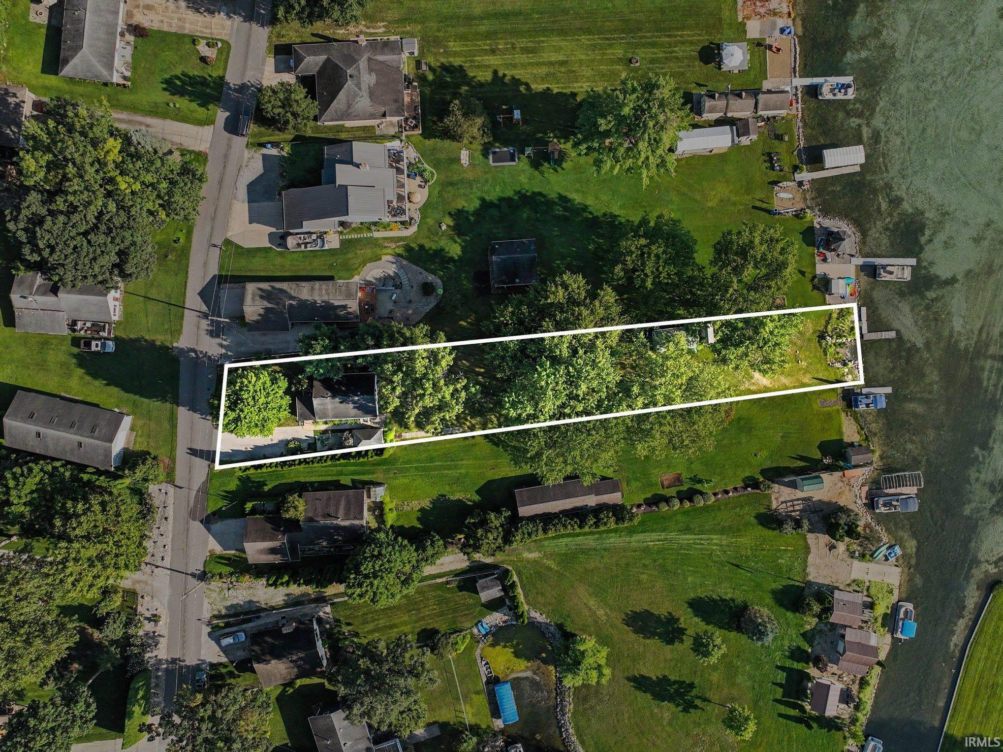Aerial property showcasing a long, narrow lot with mature trees extending to a waterfront