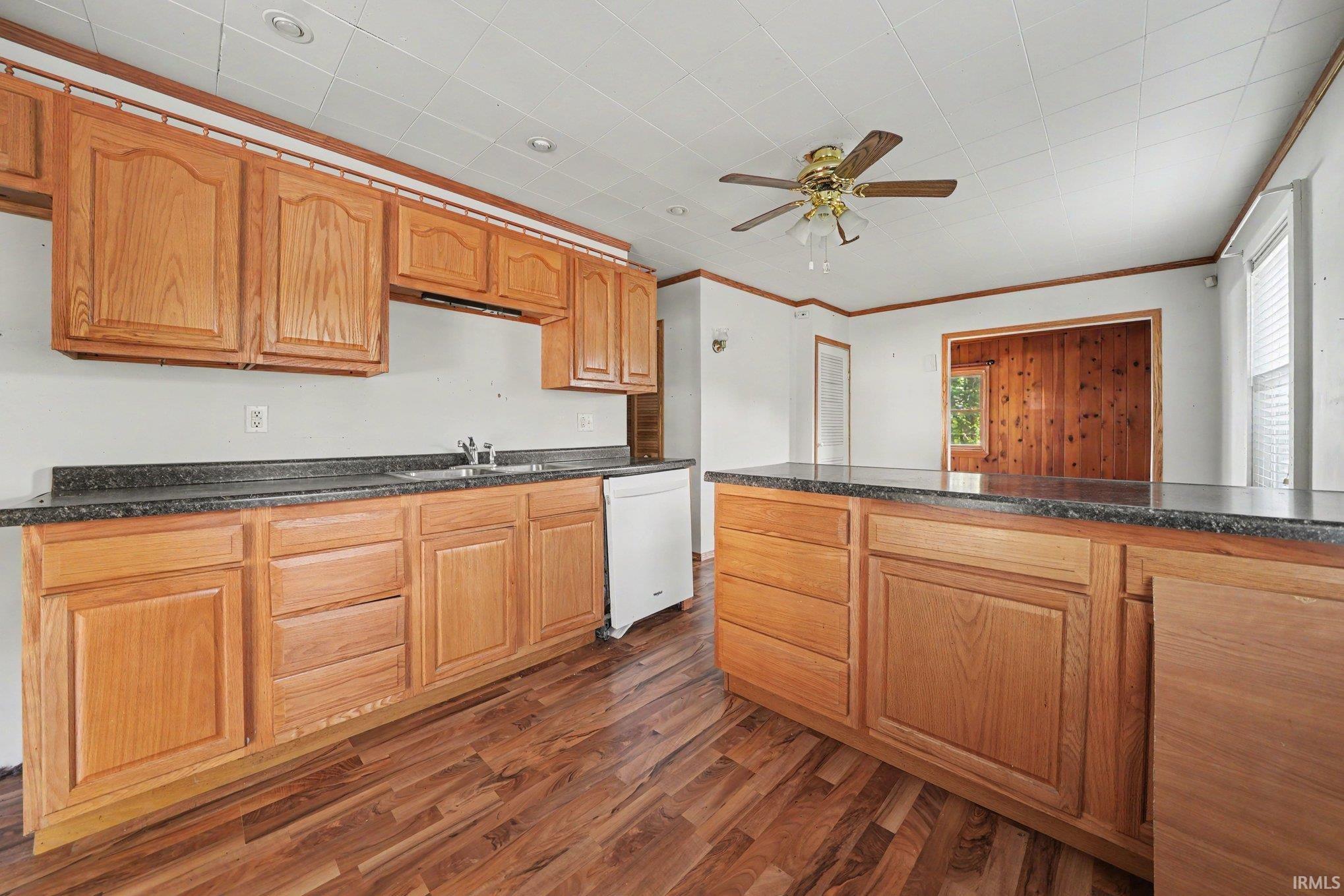 Kitchen featuring wood-finish cabinetry, dark countertops, a double basin sink, and a built-in dishwasher