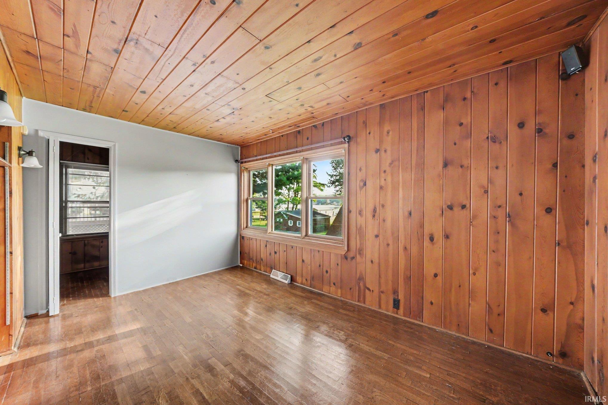 Room featuring wood-paneled walls and ceiling, wood-finish flooring, and a multi-pane window