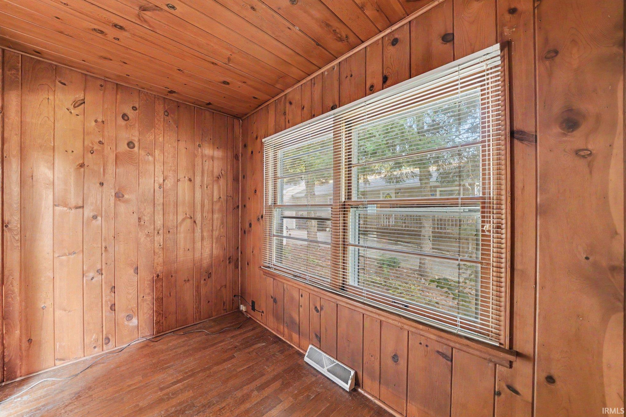 Interior room featuring wood paneling walls and ceiling, wood-finish flooring, and a multi-pane window with horizontal blinds