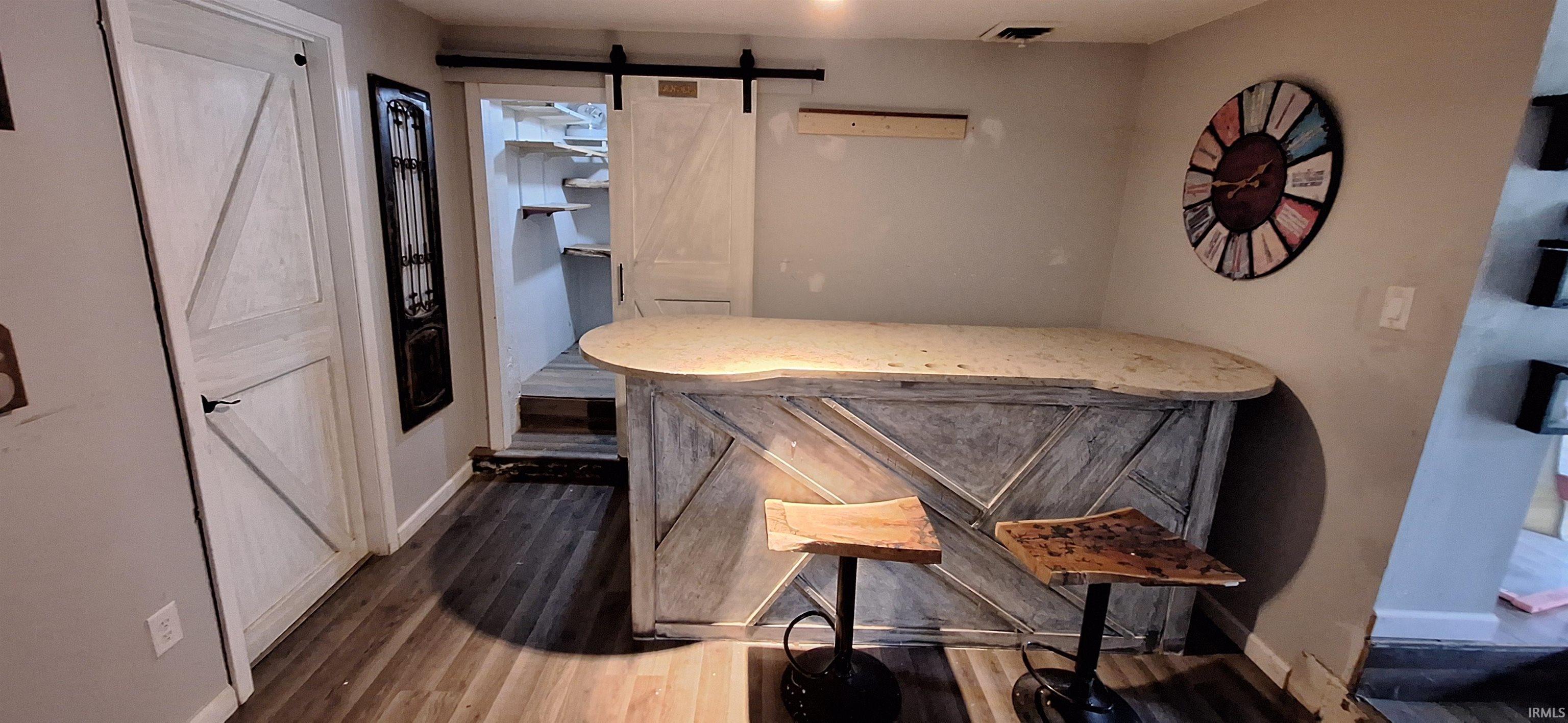 Custom-built bar with a light-toned countertop, wood-finish flooring, barn-style sliding door, and additional interior door