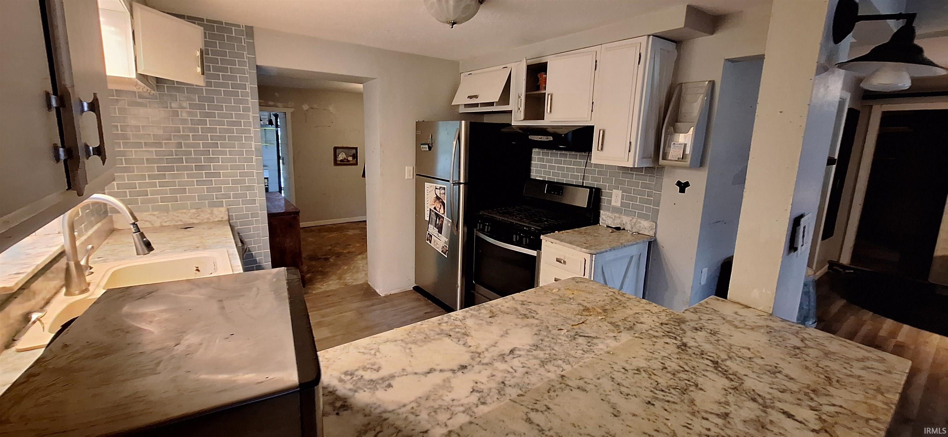 Kitchen featuring light-toned countertops, white cabinetry, a subway tile backsplash, stainless steel appliances, and wood-finish flooring
