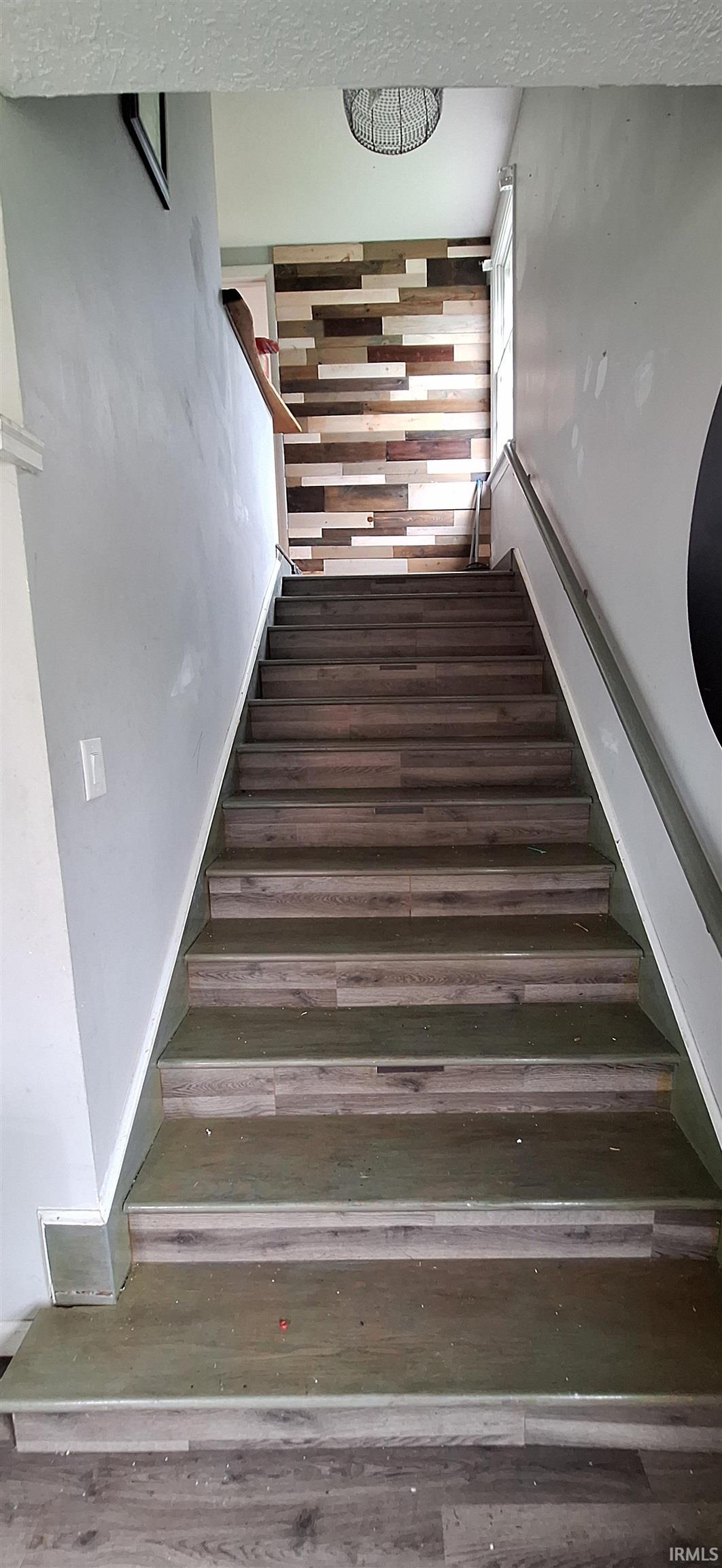 Staircase featuring wood-finish treads and risers, a wood-slat accent wall, and a linear handrail
