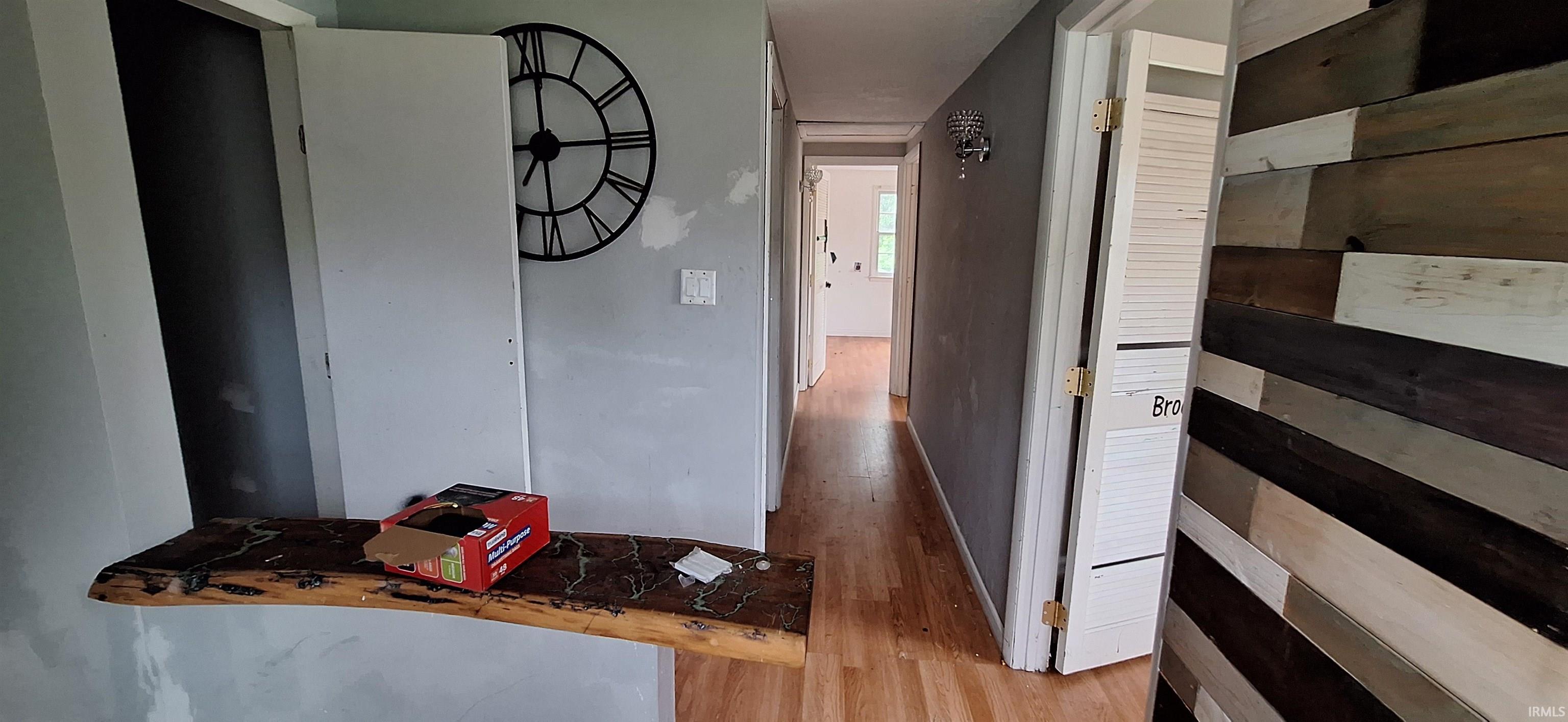 Hallway featuring wood-finish flooring, light gray walls, a decorative wall-mounted clock, and a unique wood-plank accent wall
