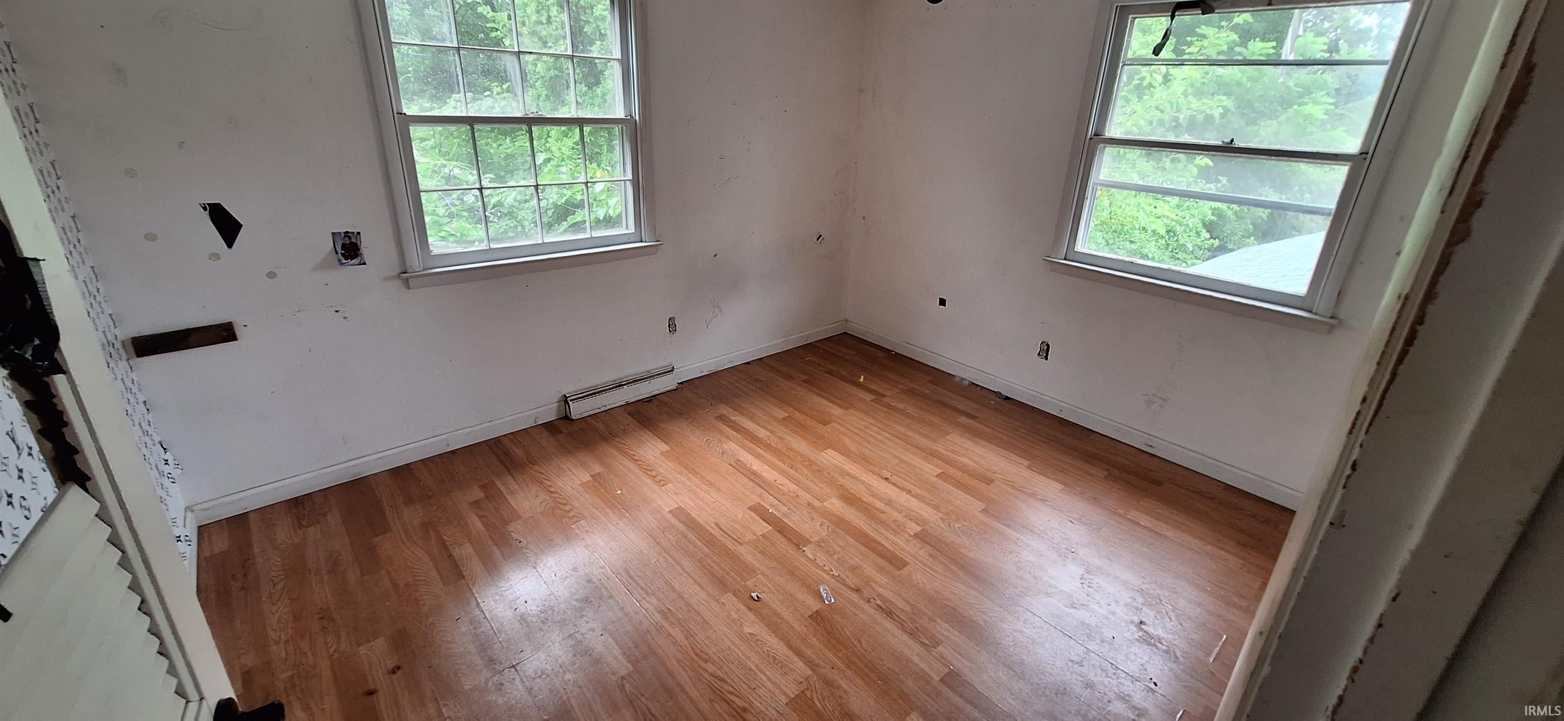 Room featuring wood-finish flooring, white baseboards, and two windows