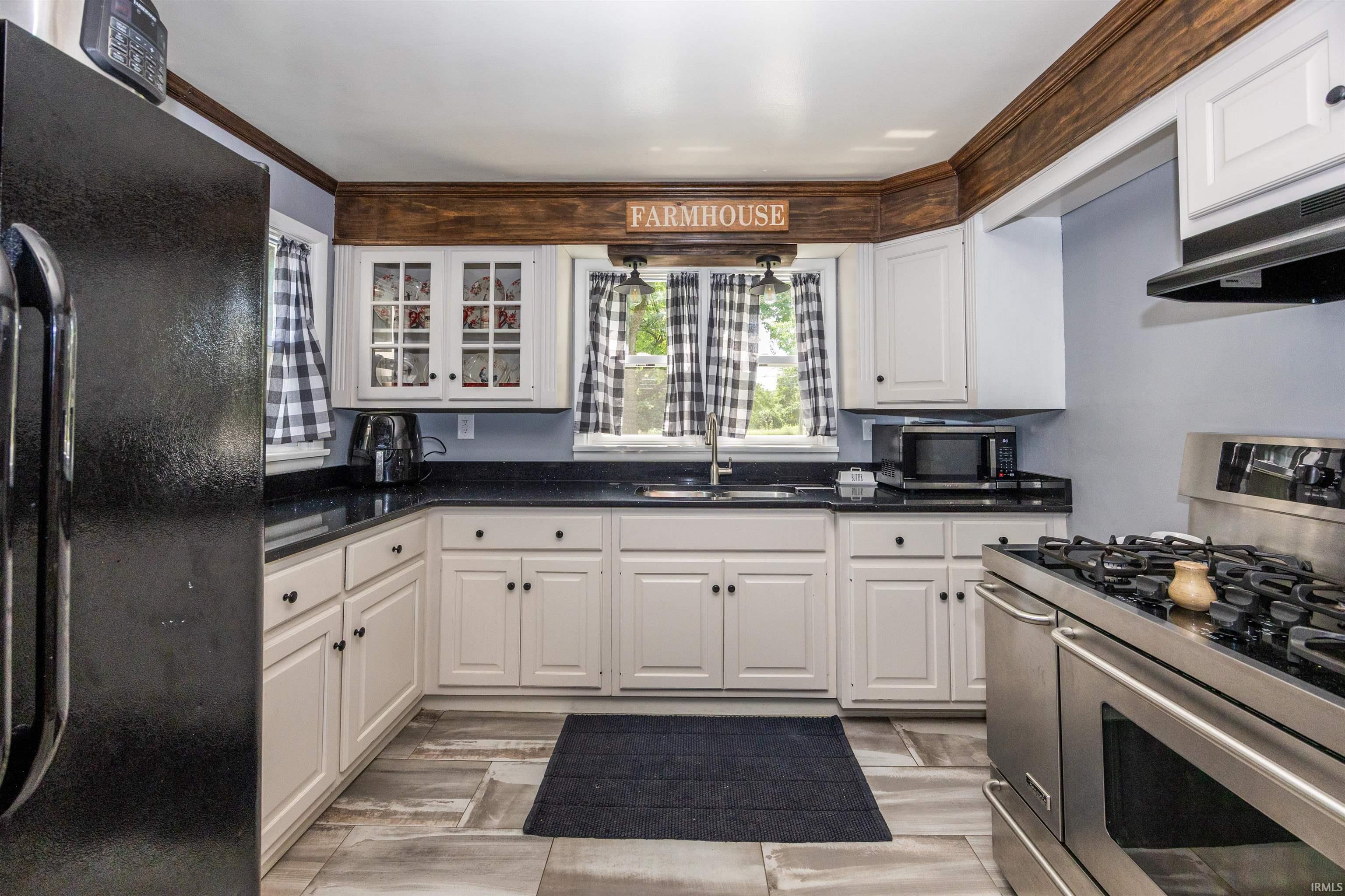 Kitchen featuring white cabinetry, dark countertops, wood-finish crown molding, tile flooring, and a stainless-steel range