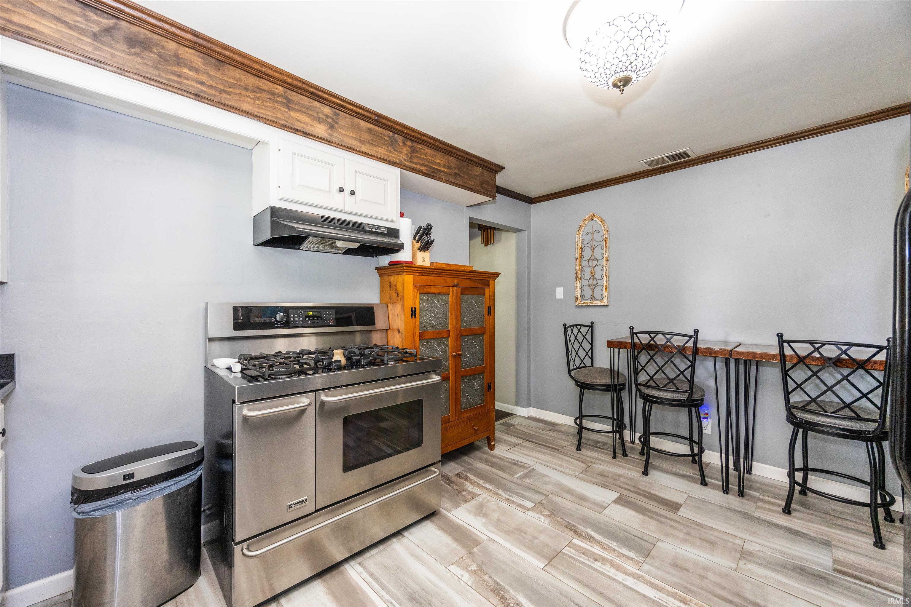 Kitchen featuring a stainless steel gas range with a matching range hood, light wood-finish flooring, and a decorative wood beam