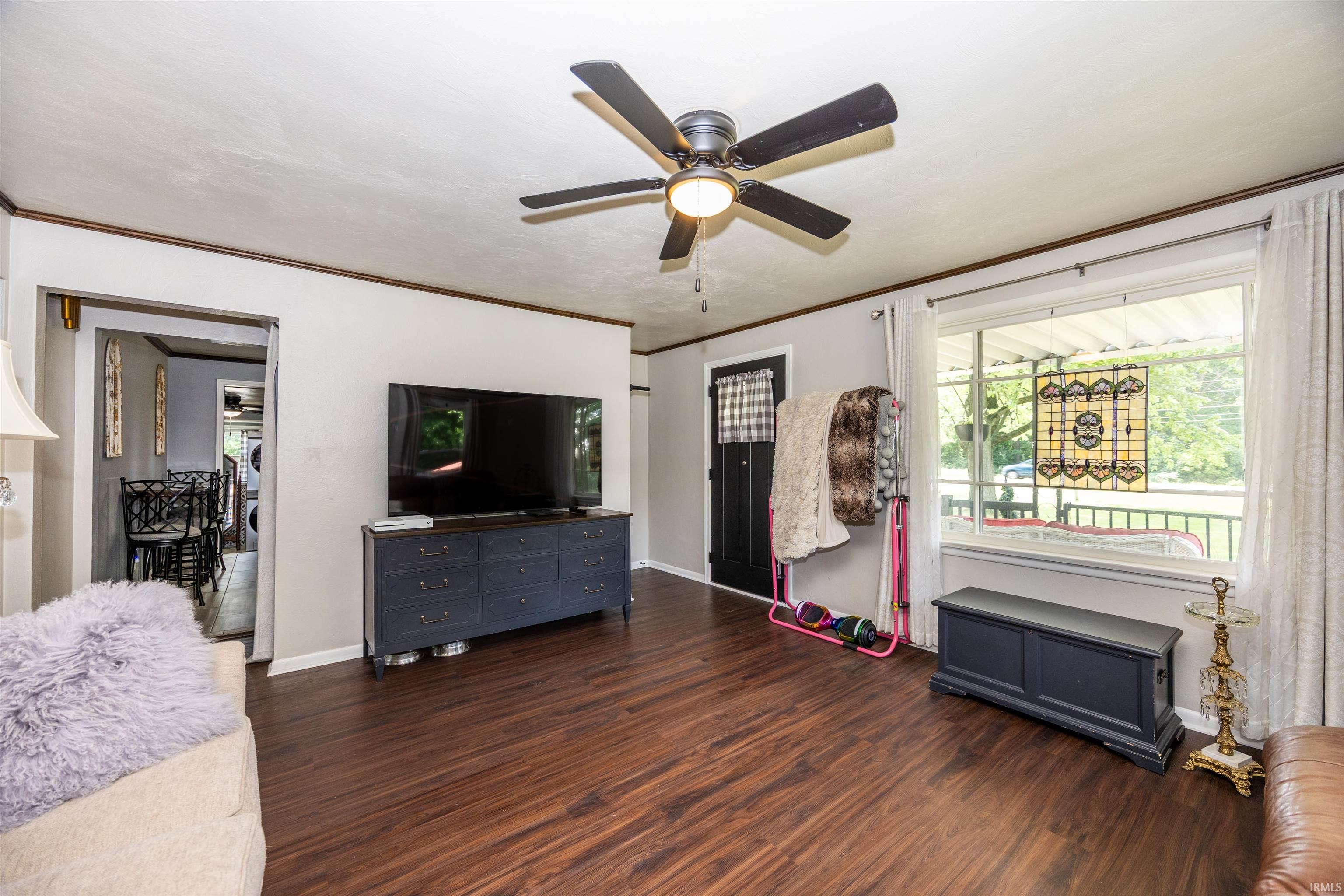 Spacious living area featuring wood-finish flooring, a ceiling fan with integrated lighting, and a large front-facing window