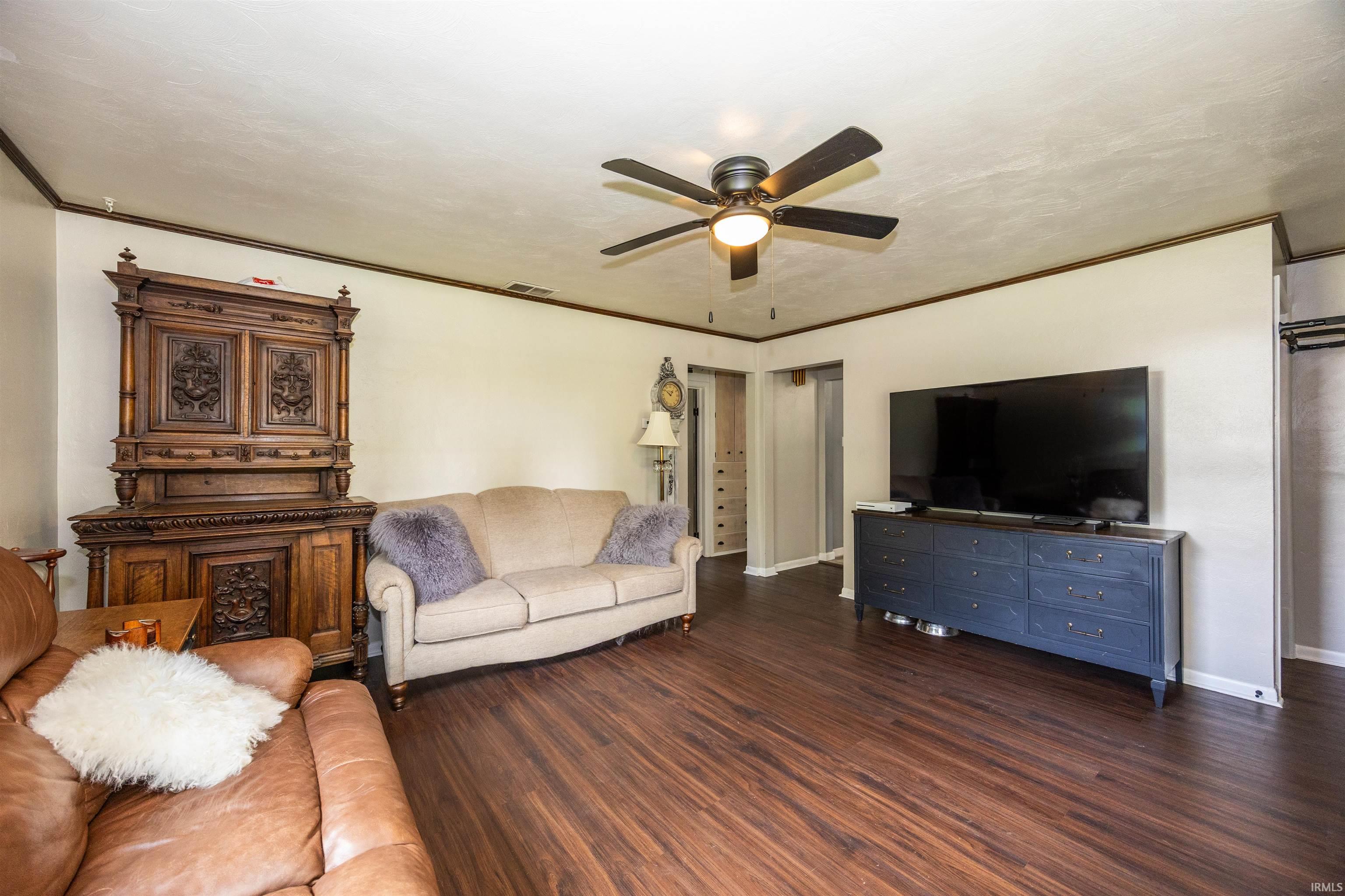 Spacious interior featuring wood-finish flooring, a ceiling fan with integrated lighting, and crown molding