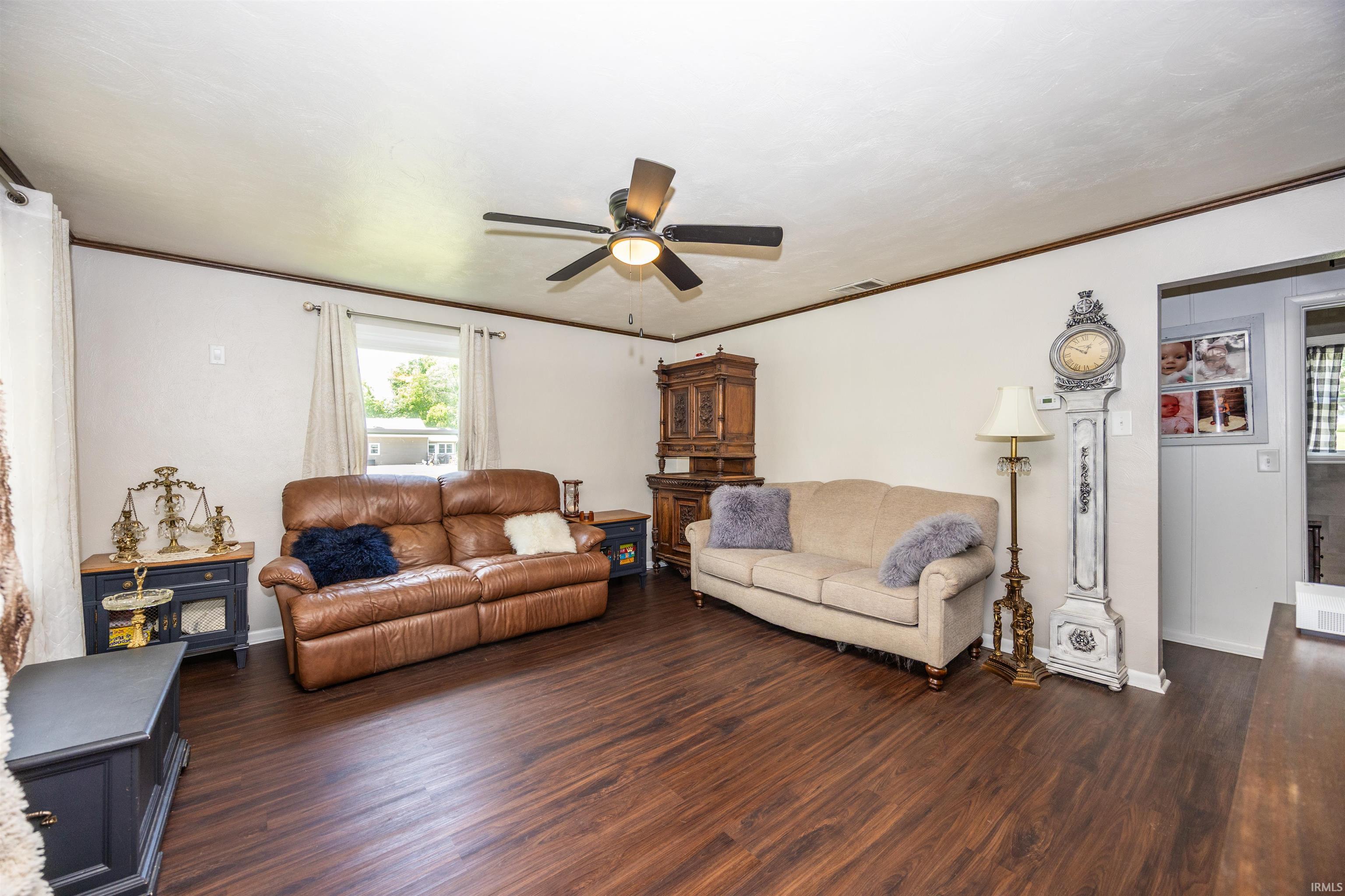 Spacious living area featuring wood-finish flooring, white walls with dark trim, a ceiling fan with integrated lighting, and multiple windows providing natural light