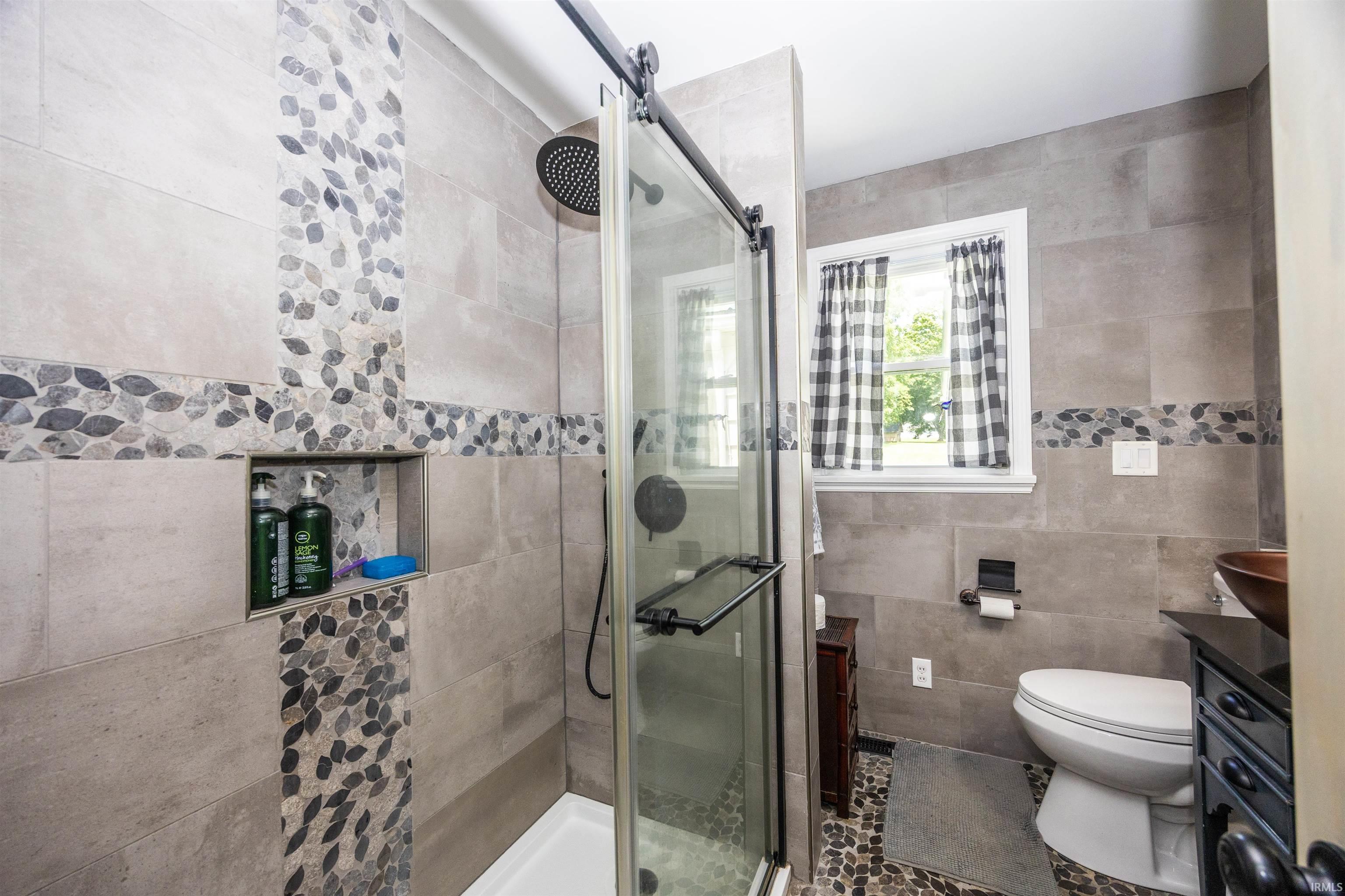 Shower enclosure with sliding glass door, mosaic tile accents, recessed shower niche, pebble floor, and wall-mounted shower head