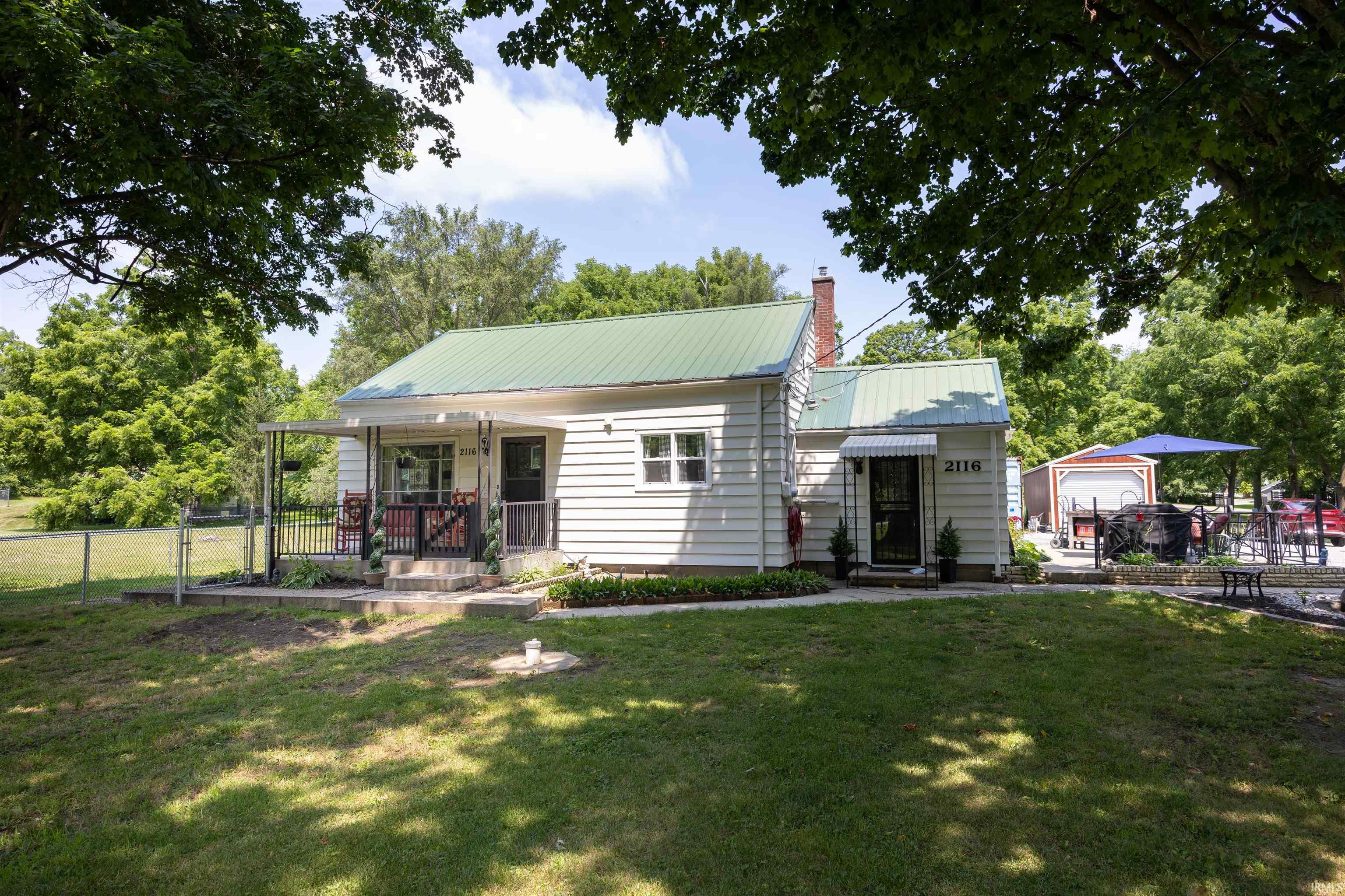 Charming white siding residence featuring a green metal roof and front porch with wrought iron railing