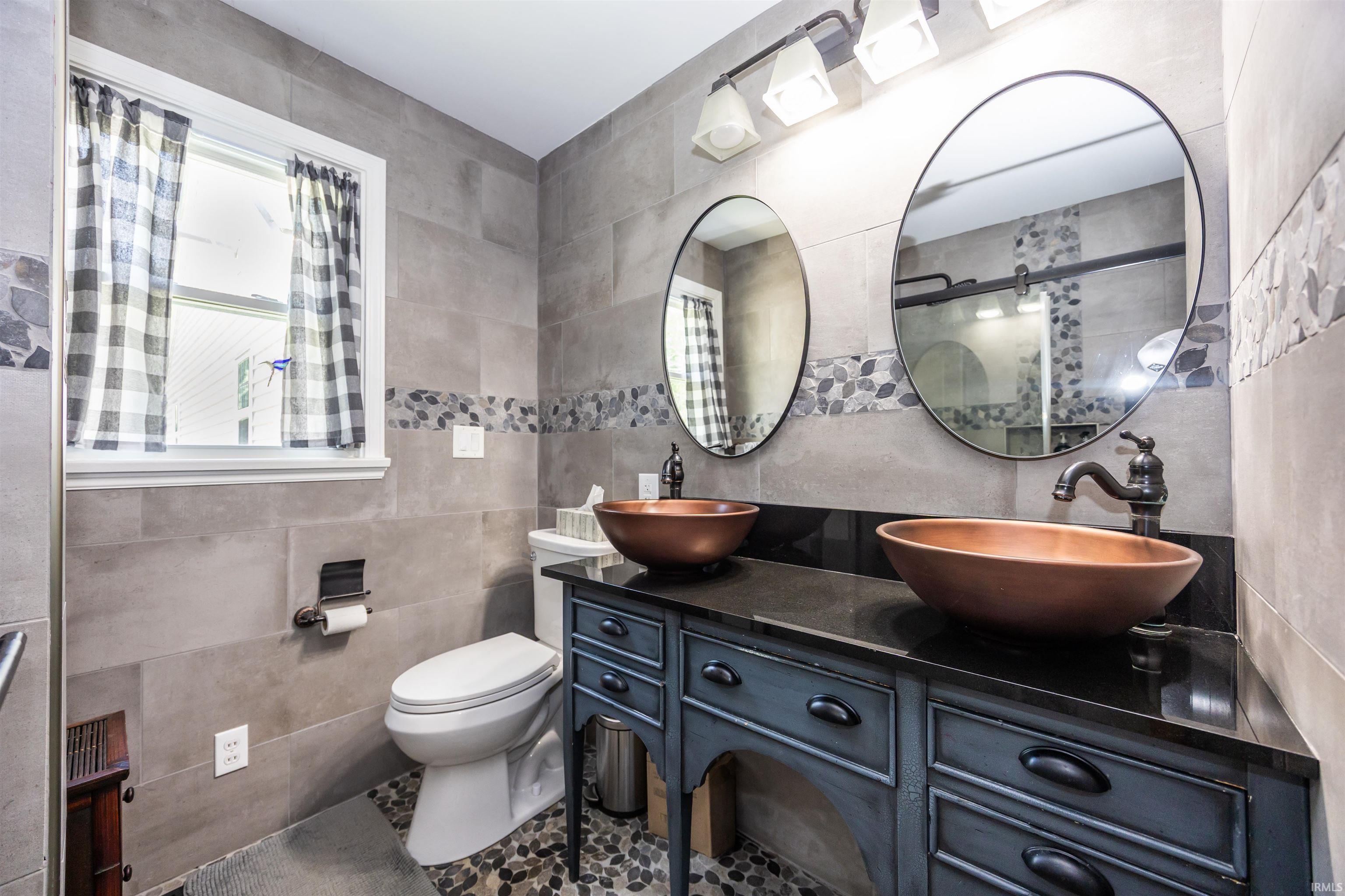 Dual copper vessel sinks set on a dark countertop with an aged-finish vanity