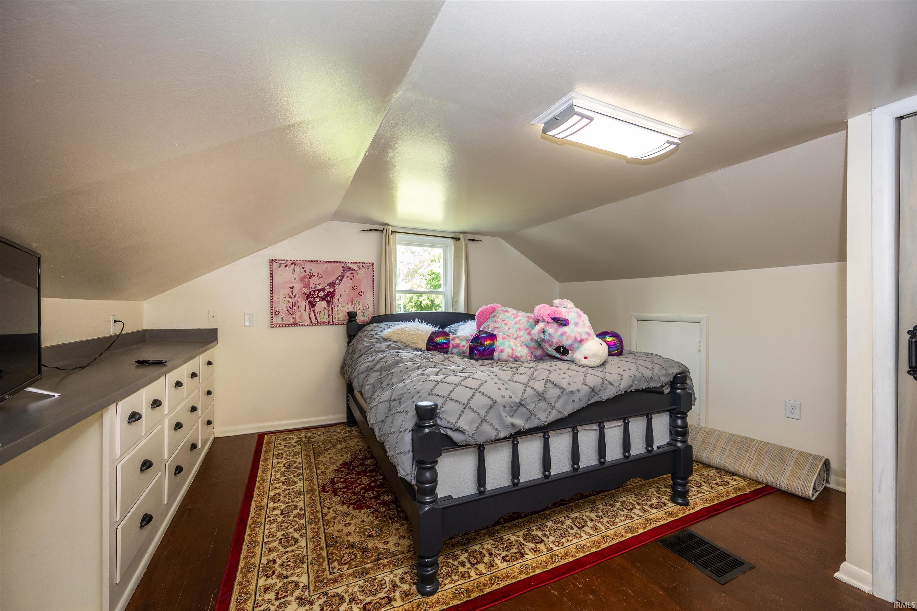 Bedroom featuring sloped ceilings, dark wood-finish flooring, and a built-in storage unit with multiple drawers and a countertop surface