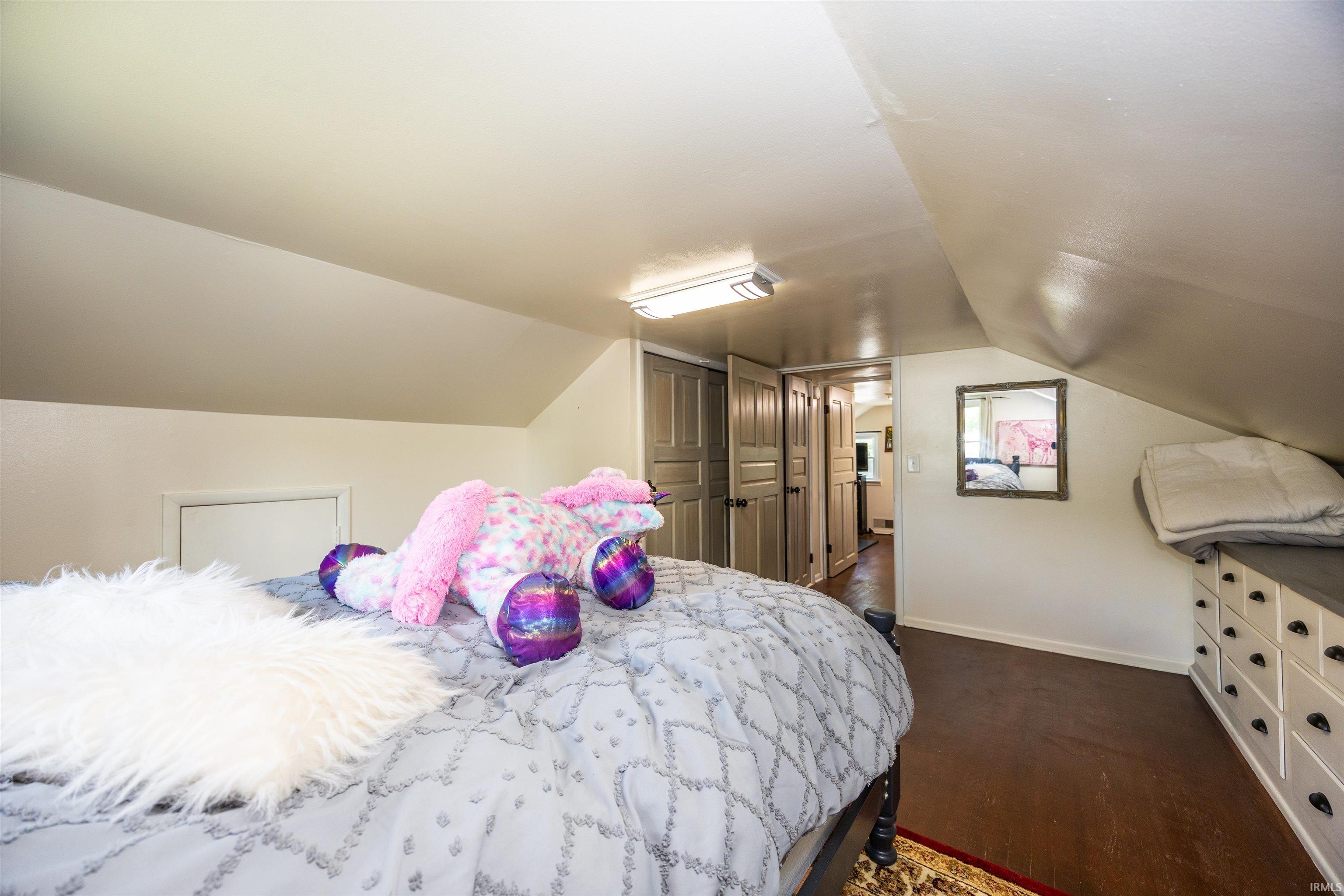 Attic room featuring sloped ceilings, wood-finish flooring, recessed storage access, built-in drawer storage, and a flush mount ceiling light fixture