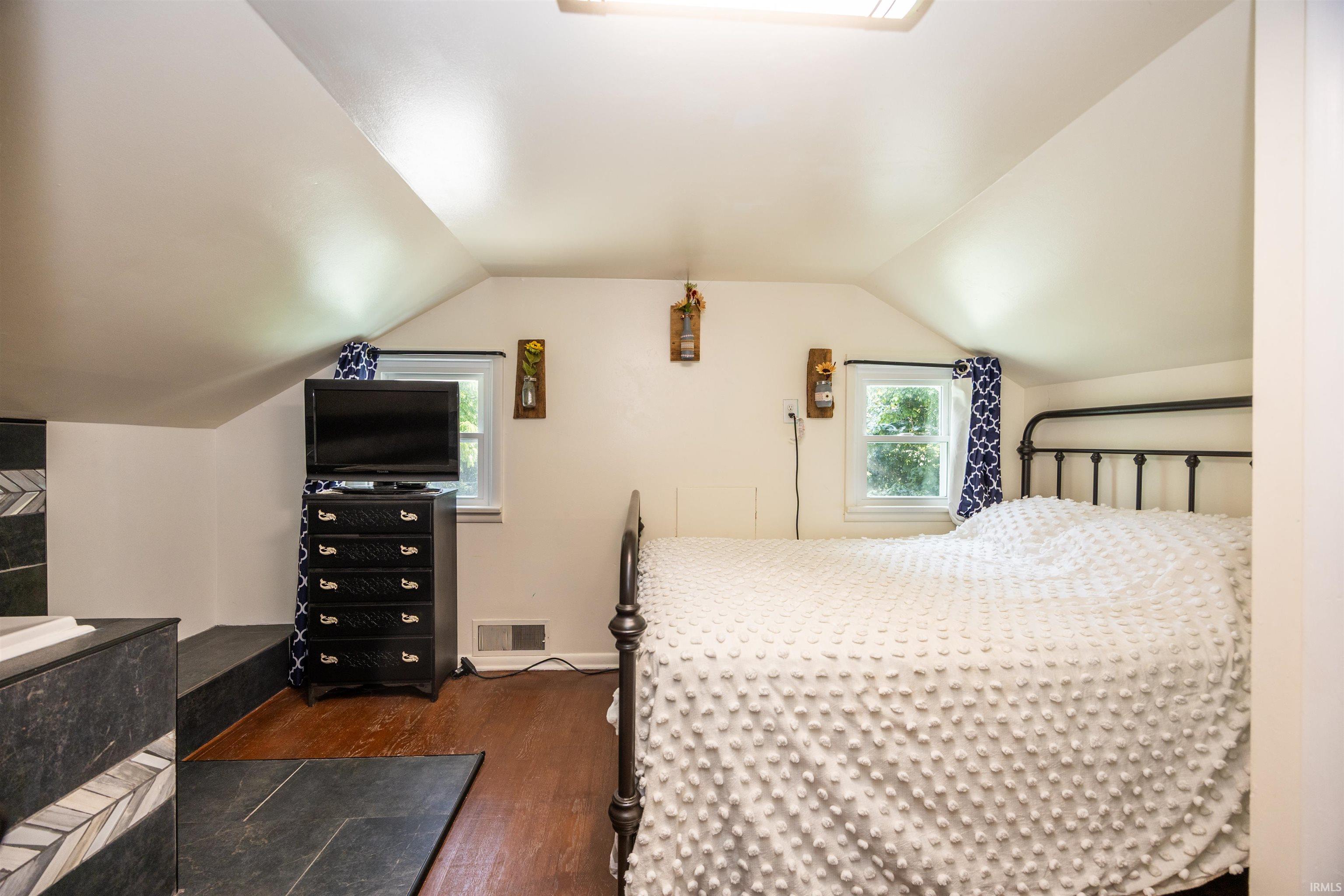 Sloped ceiling room featuring wood-finish flooring, two windows, and a built-in tiled platform with a patterned accent